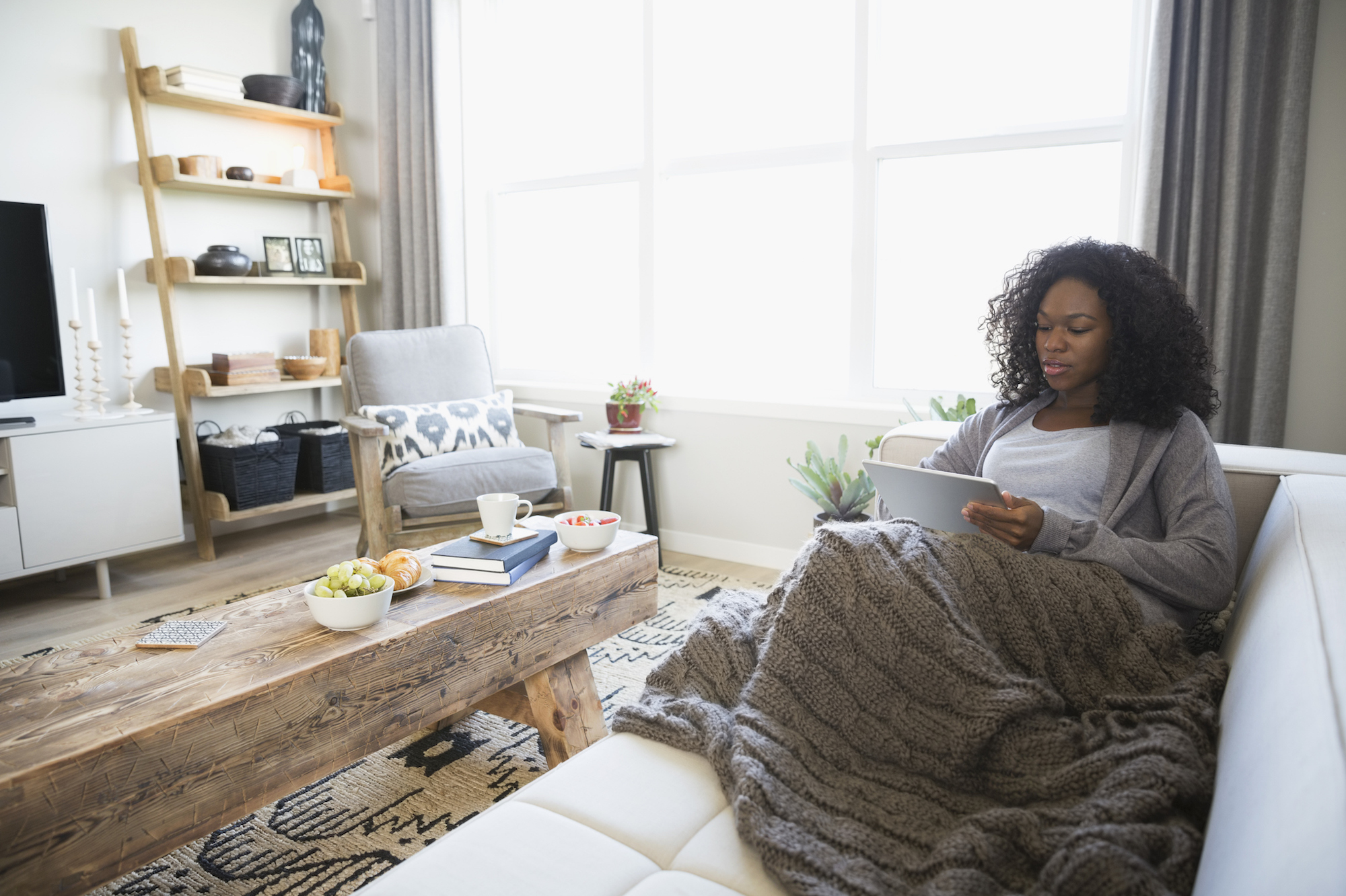 Relaxed woman with blanket using digital tablet on living room sofa