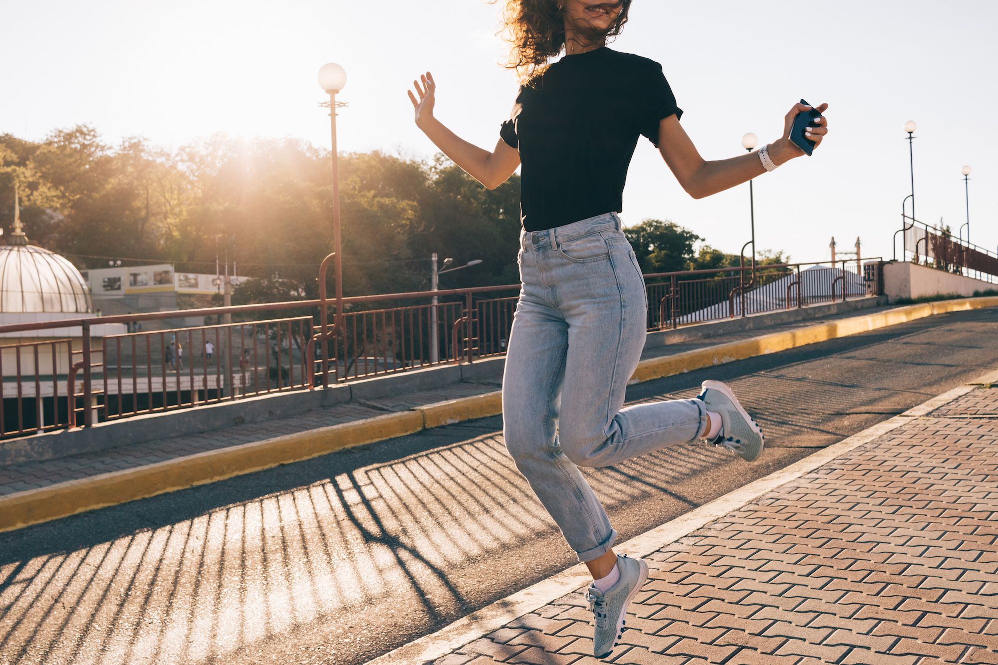 Happy girl with curly brown hair jumping in the city