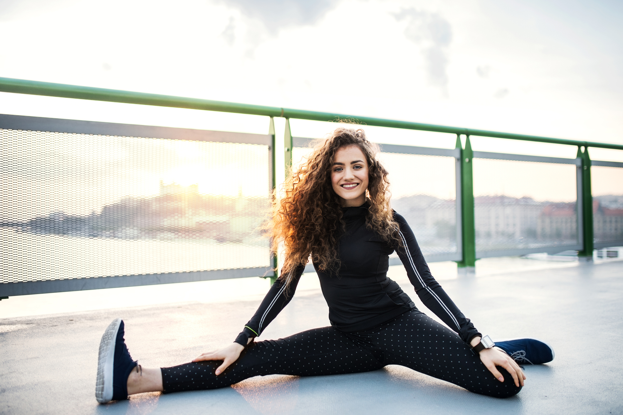 A sporty young woman stretching on the bridge outdoors in the city.