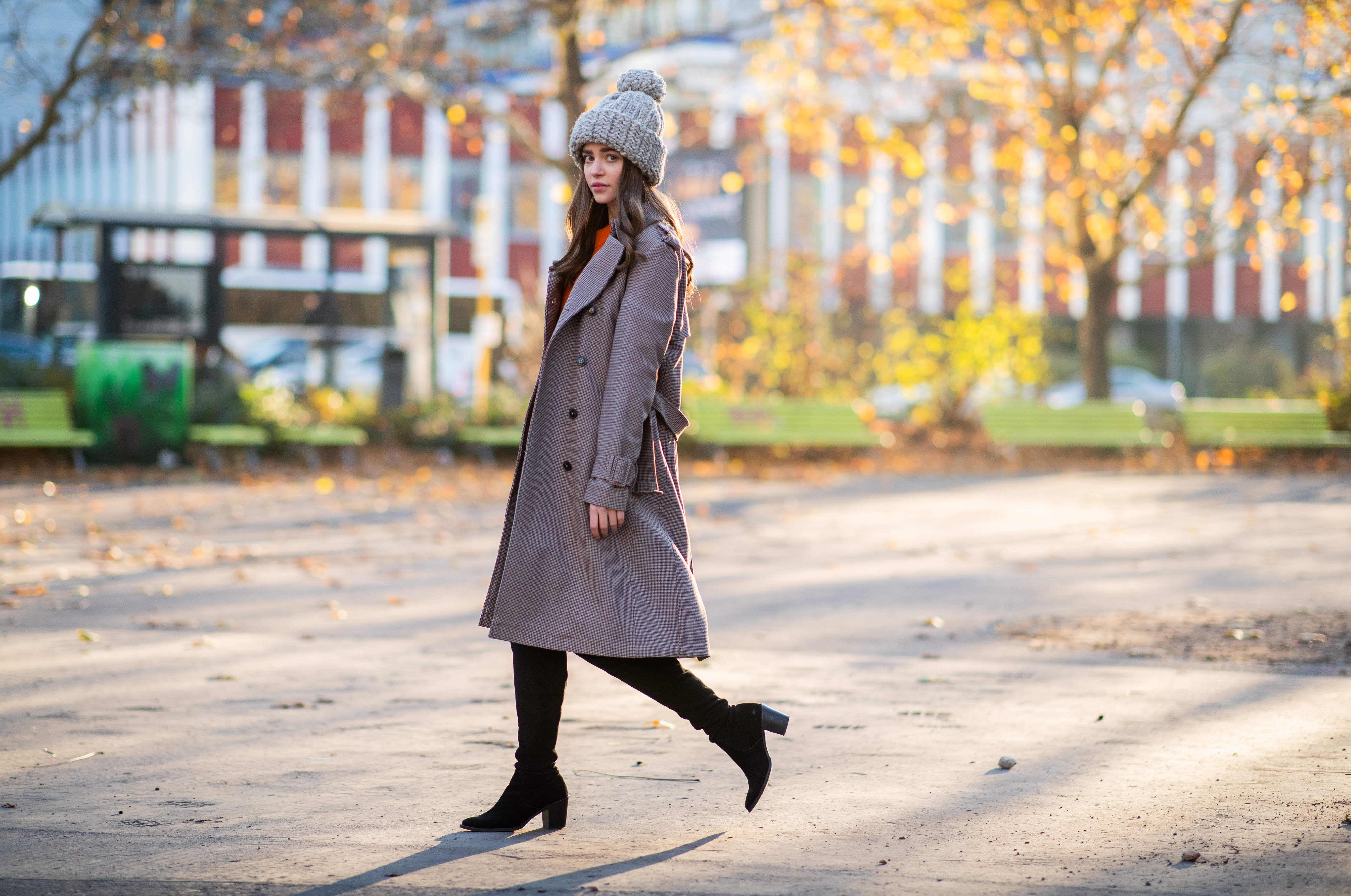 woman wearing boots, a trench coat and knit cap