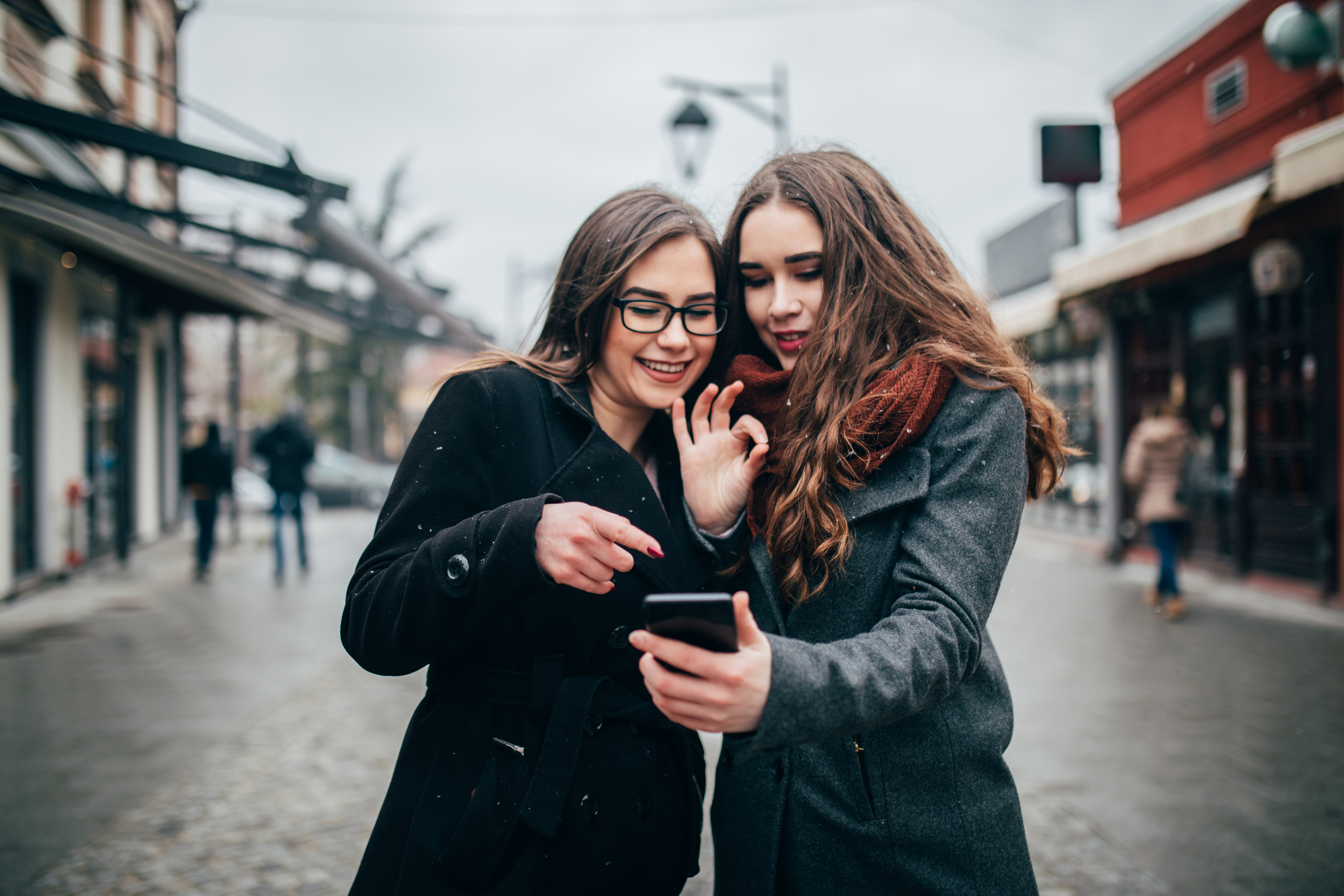 Two female friends using phone downtown