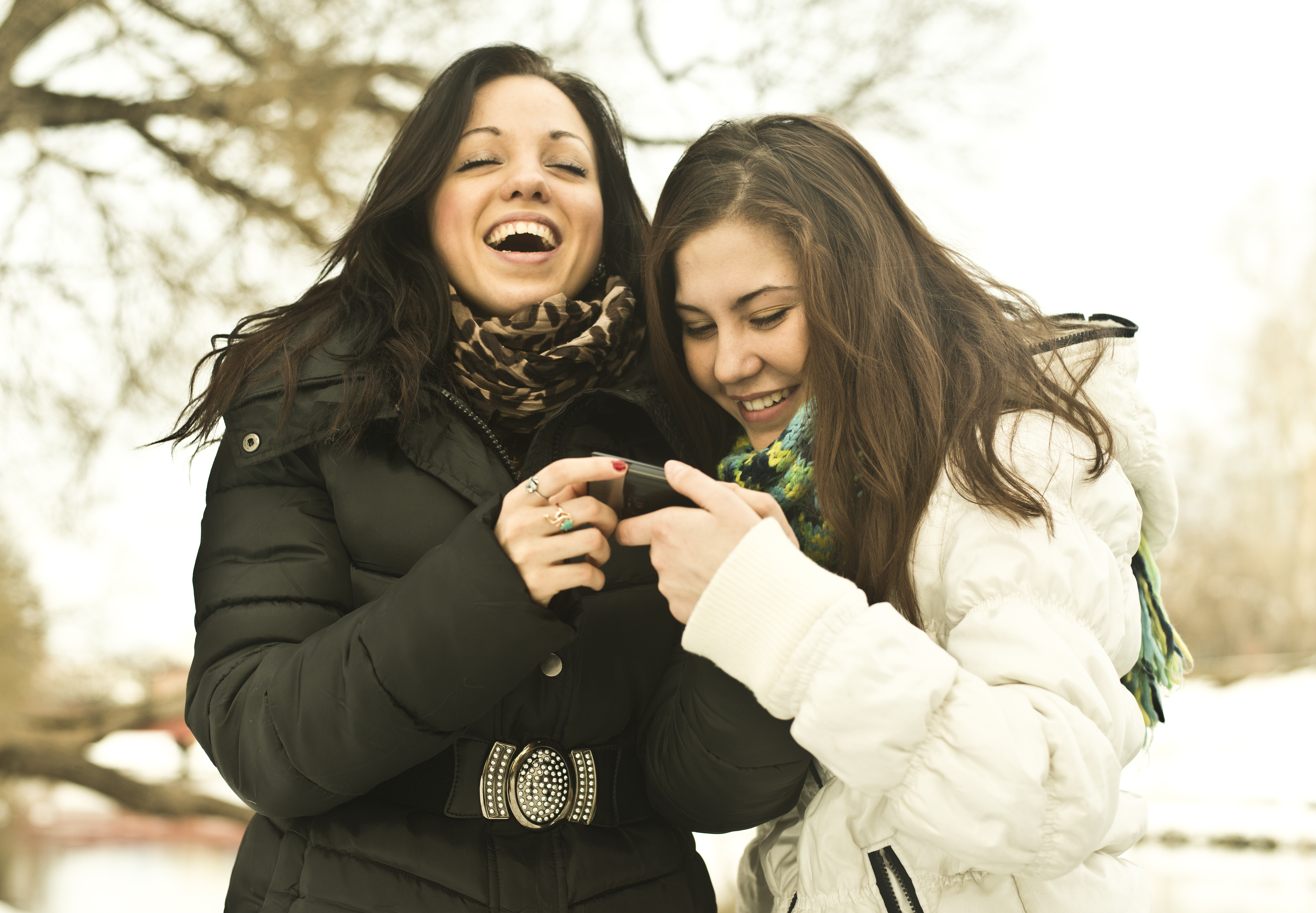 Two young women laughing at mobile phone in park in winter