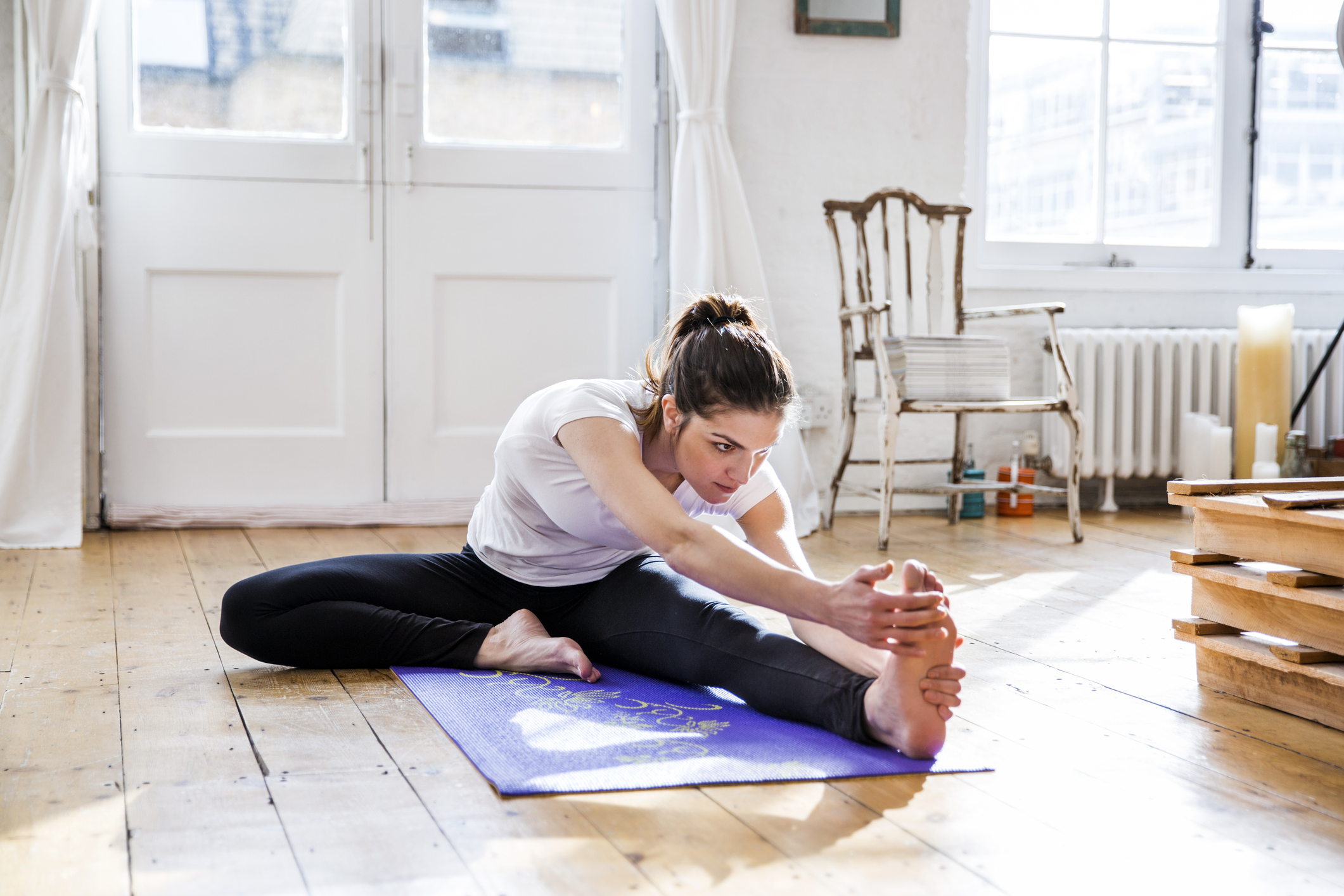 Young woman practicing yoga, touching toes in apartment