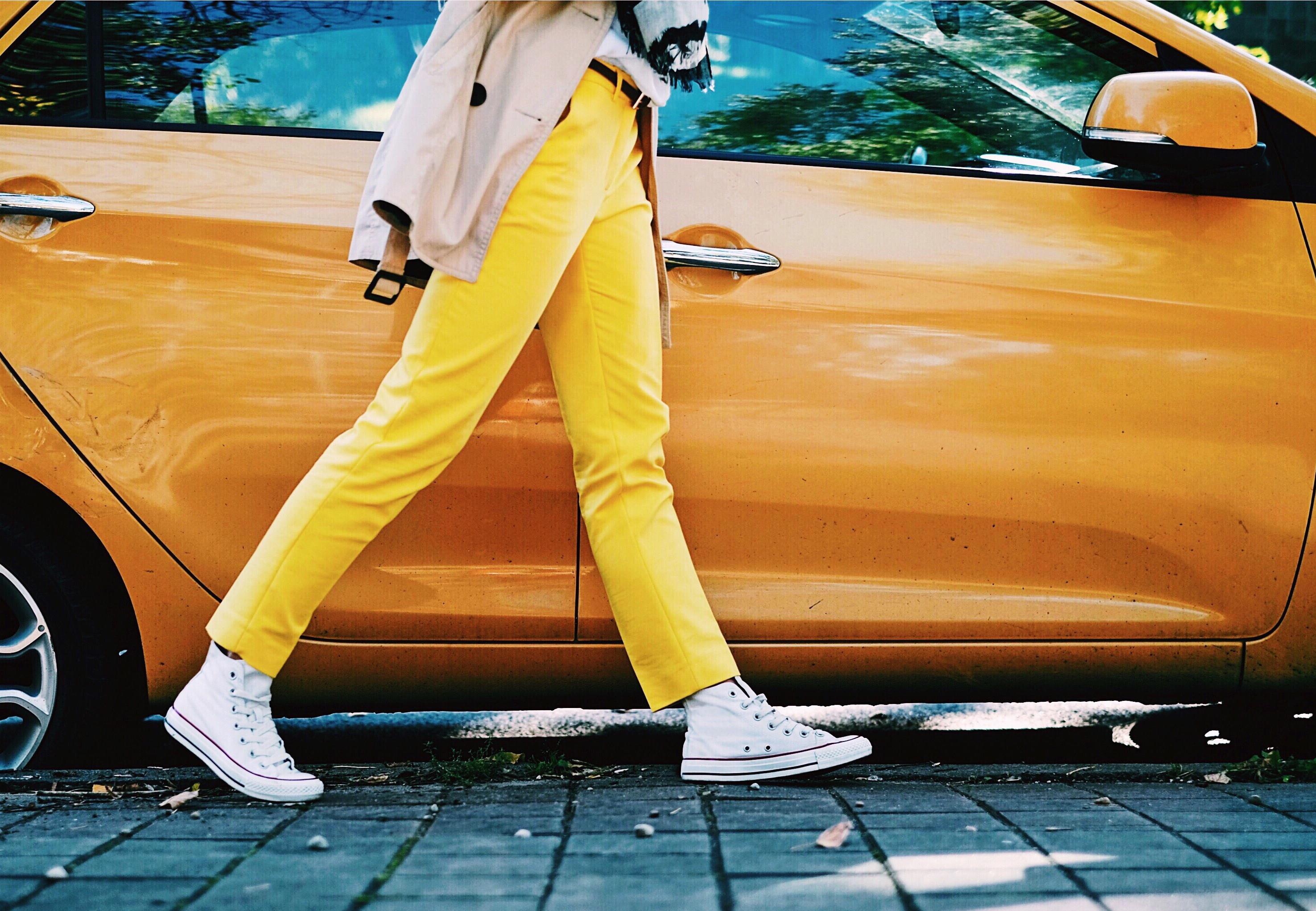 Woman in yellow trousers walking past an orange car