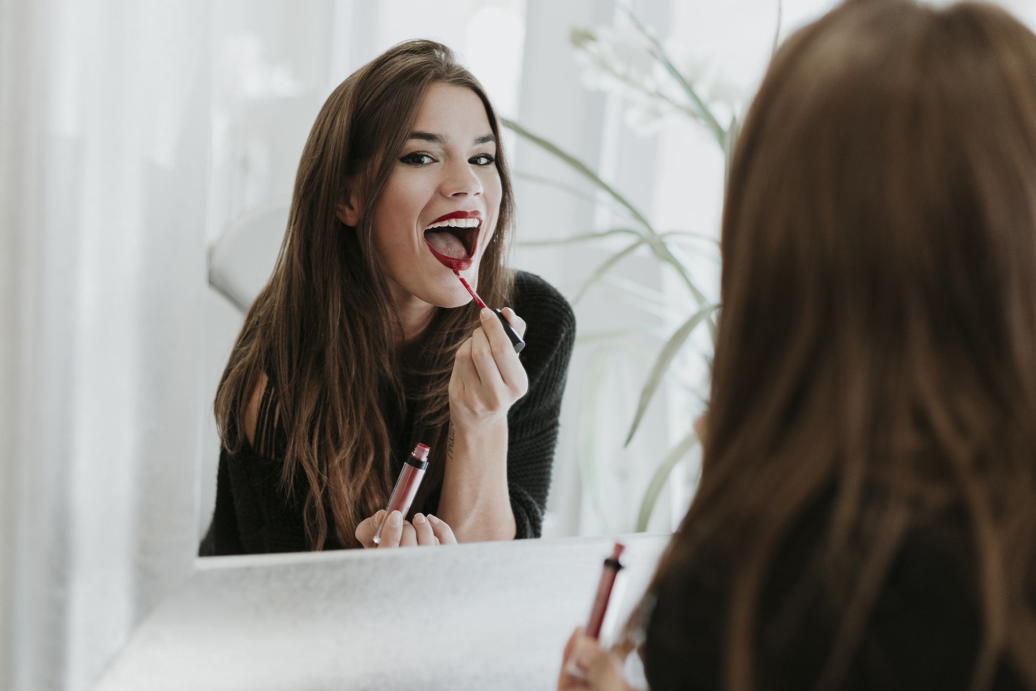 Mirror image of young woman applying lipstick