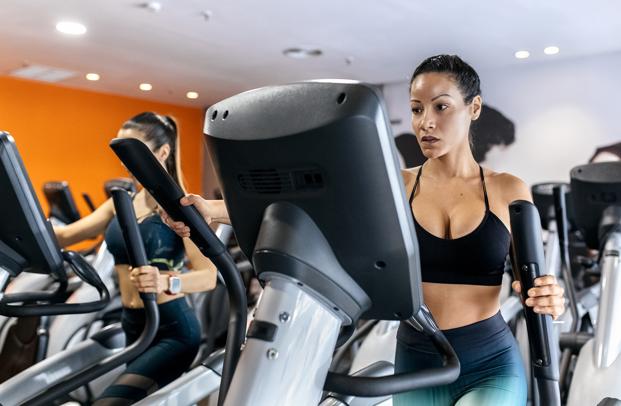 two women working out in gym using a elliptical
