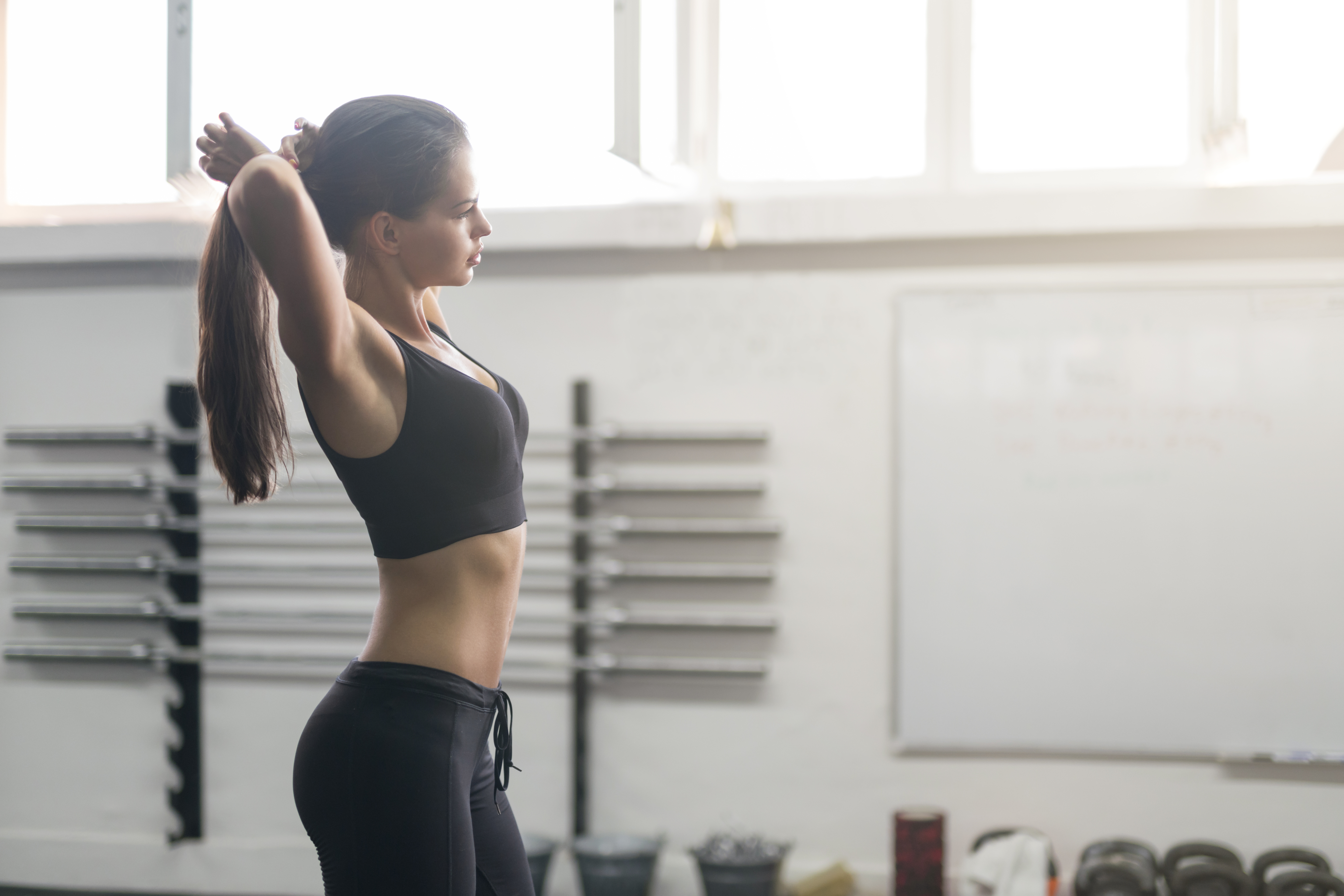 Beautiful girl in sport clothing standing in the gym and adjusting her hair, preparing for the training