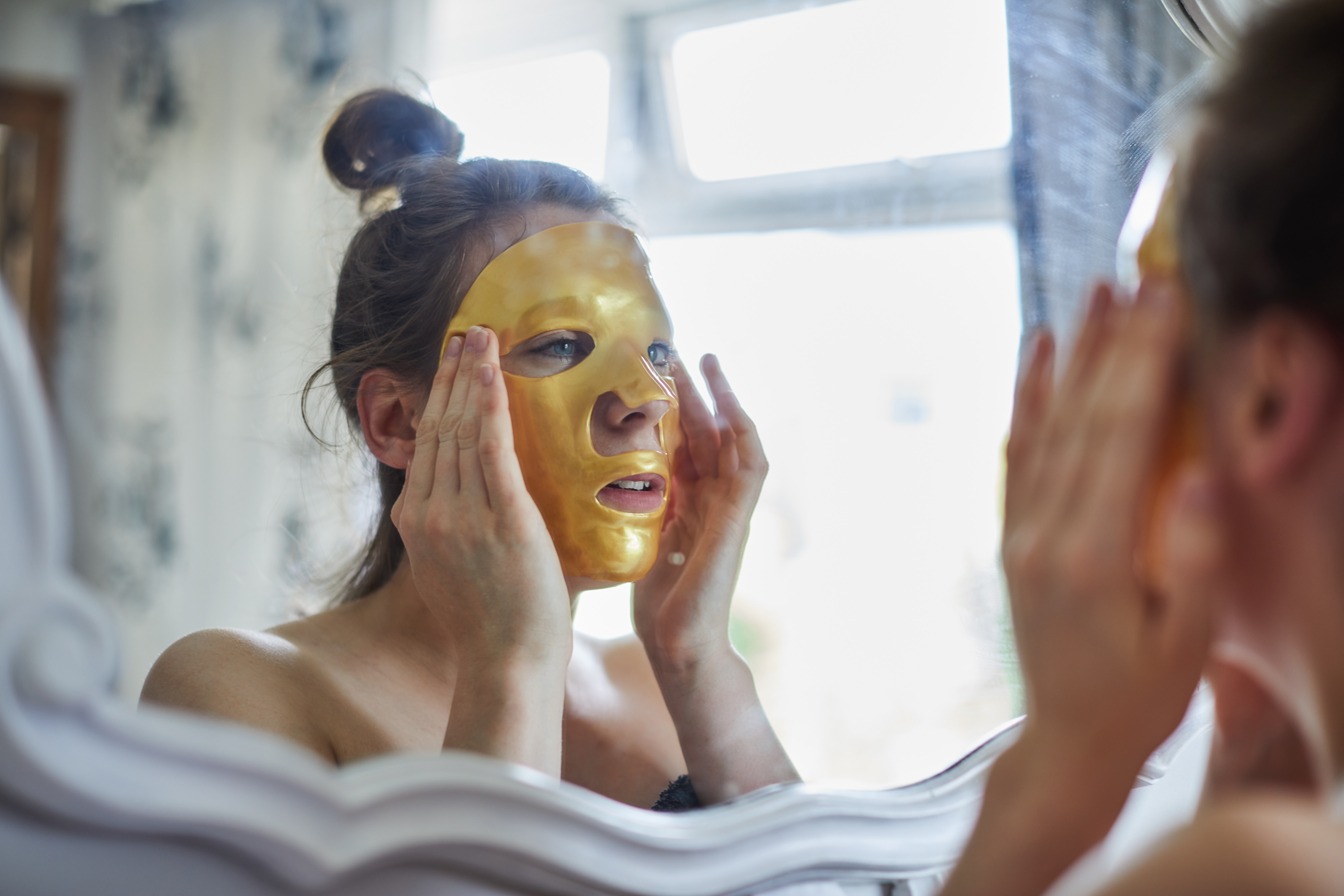 Woman applying a gold face mask in the mirror
