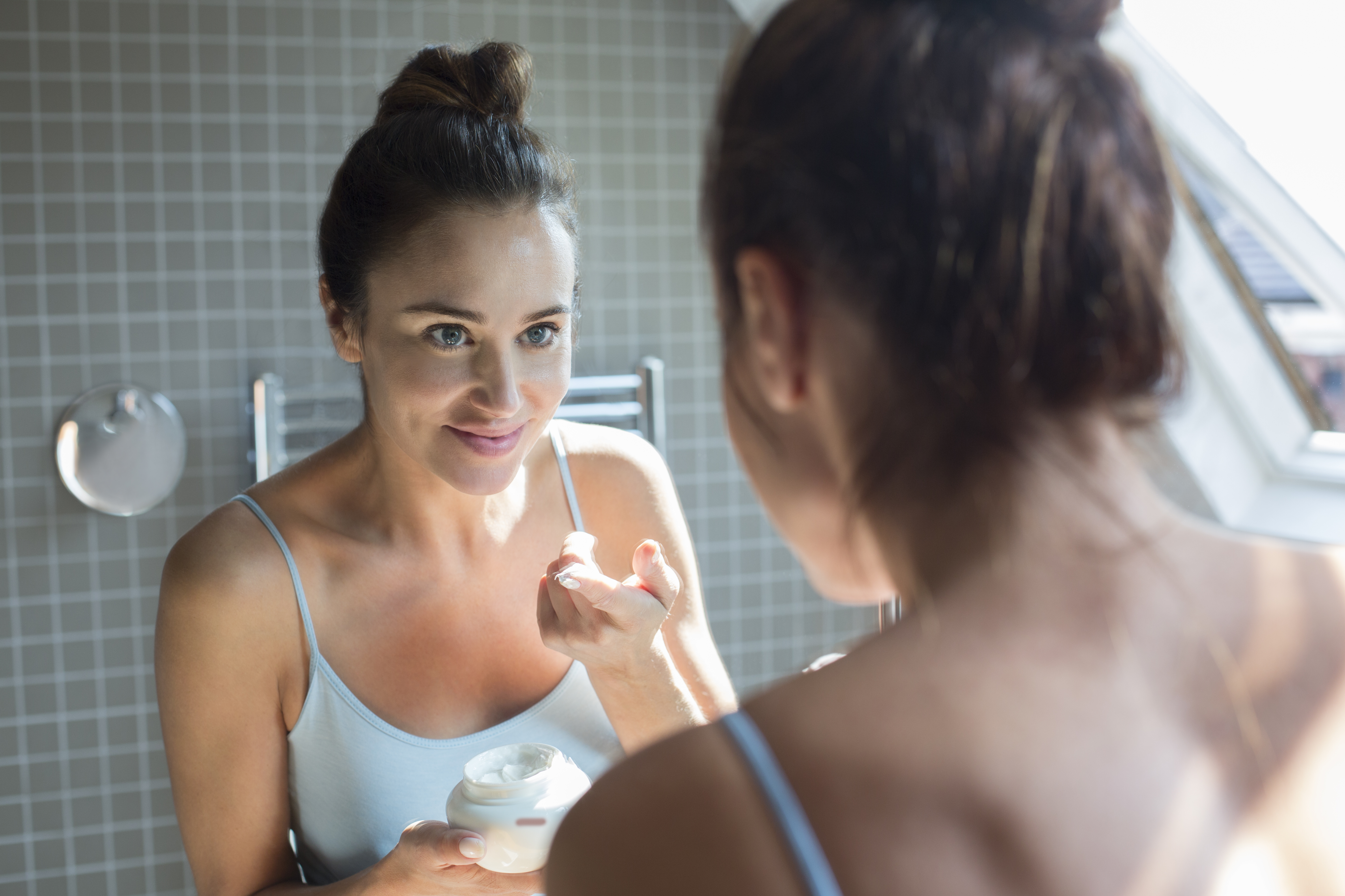 Mid adult woman applying moisturiser in bathroom.