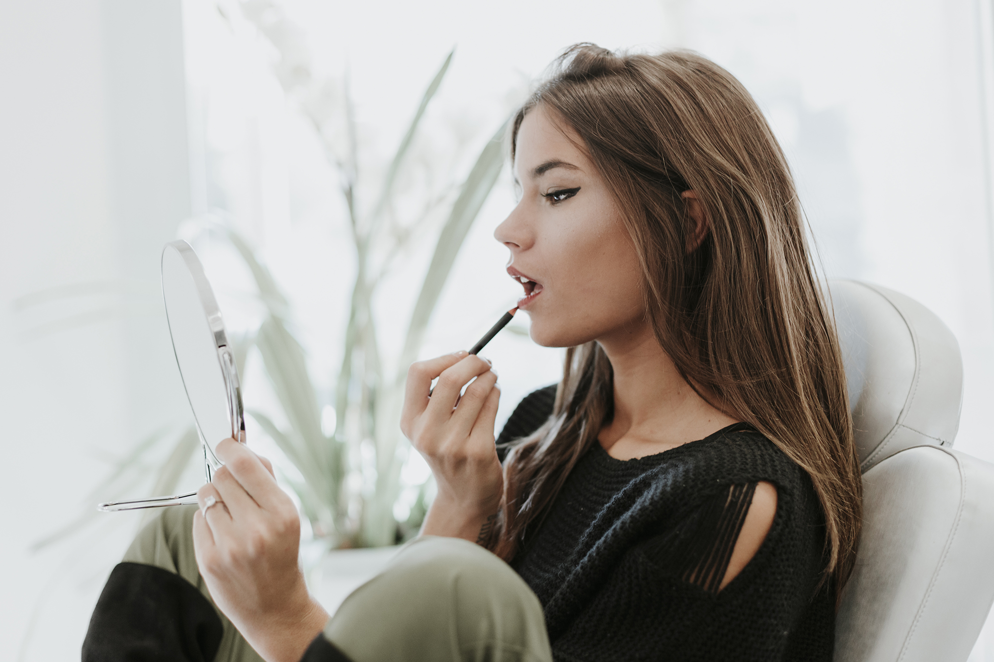 Portrait of young woman using lip pencil