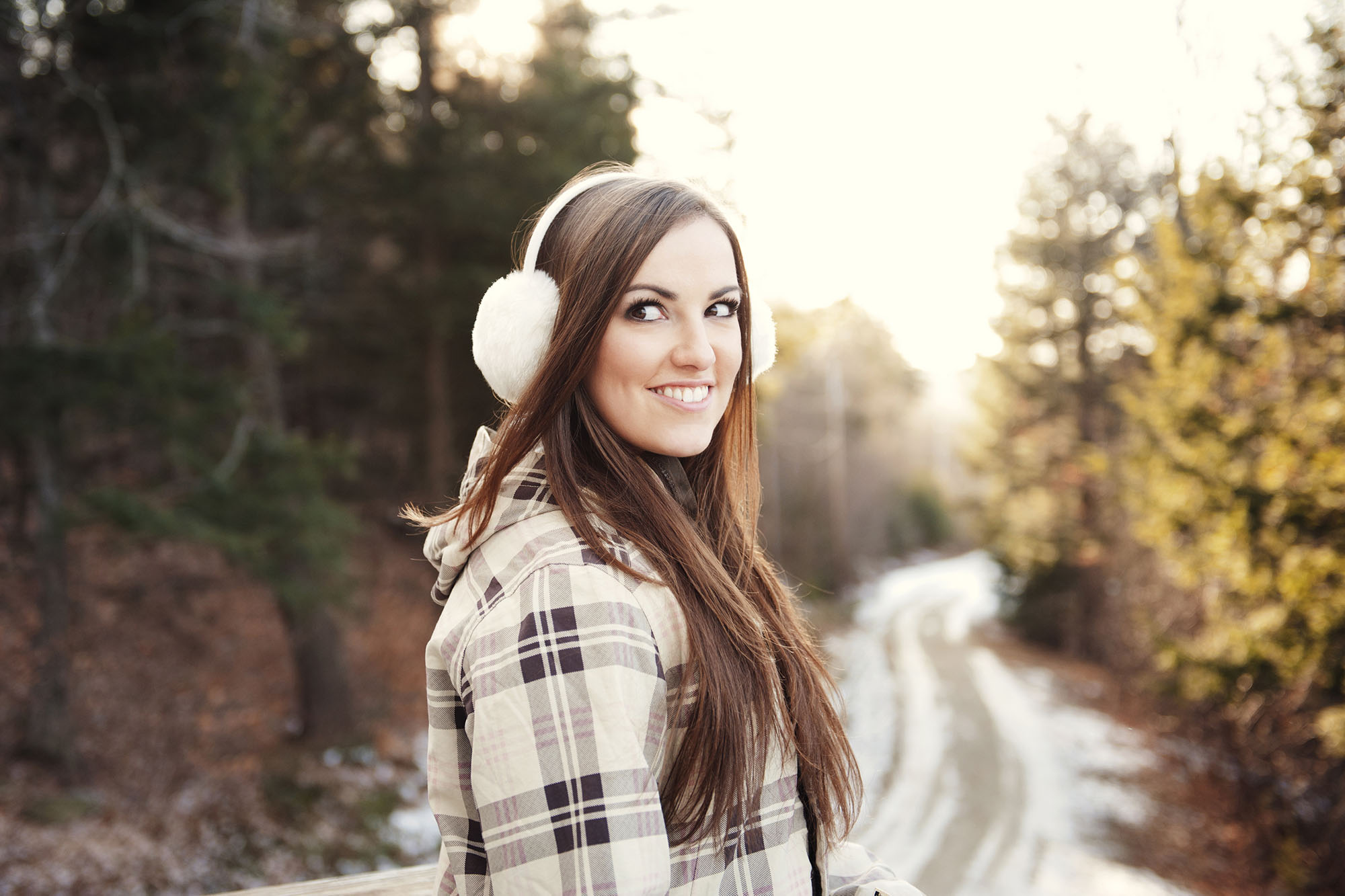 Happy woman wearing ear muff while standing on footpath during winter