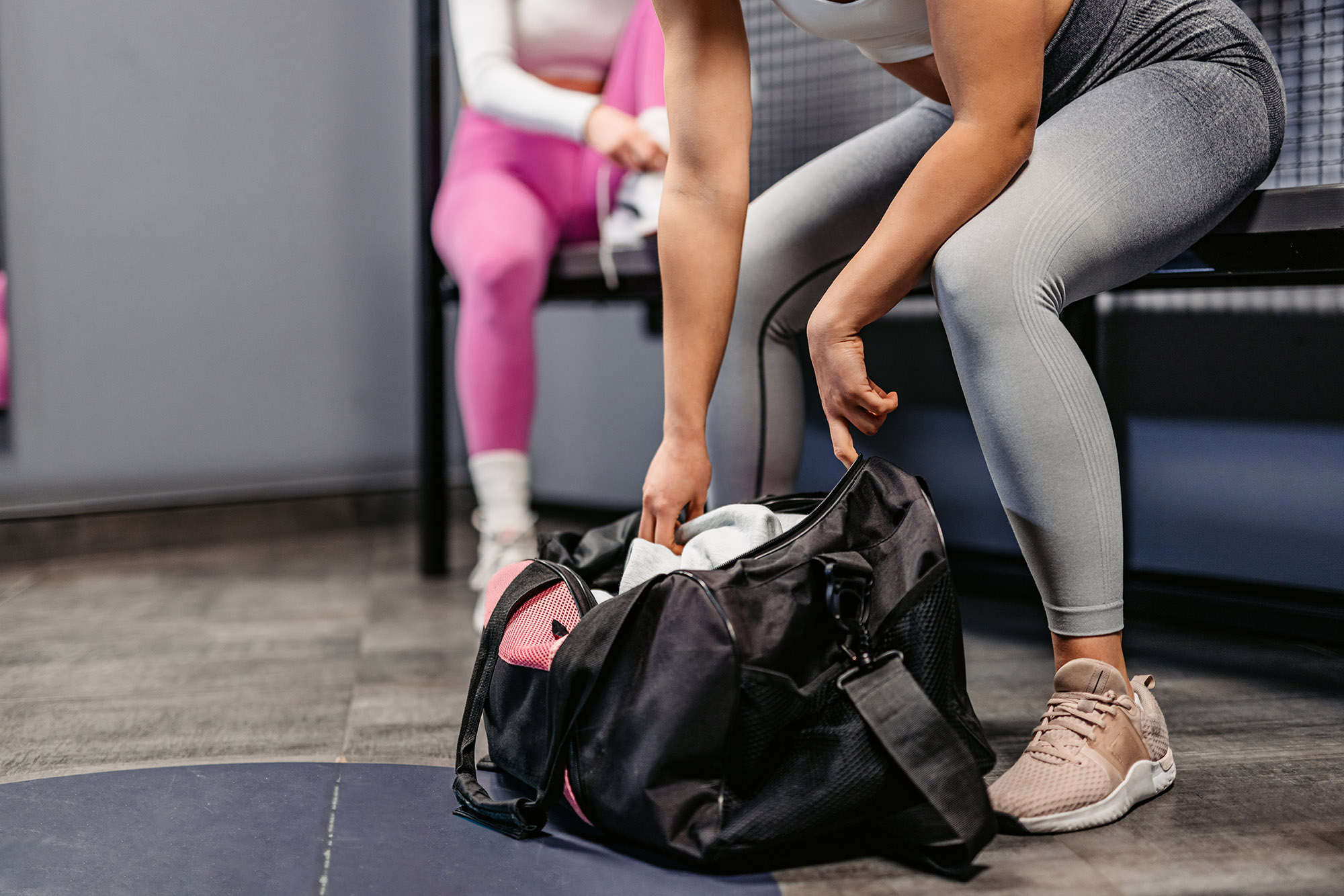 Close-up of a young athletic woman opening up her gym bag at the gym locker room.