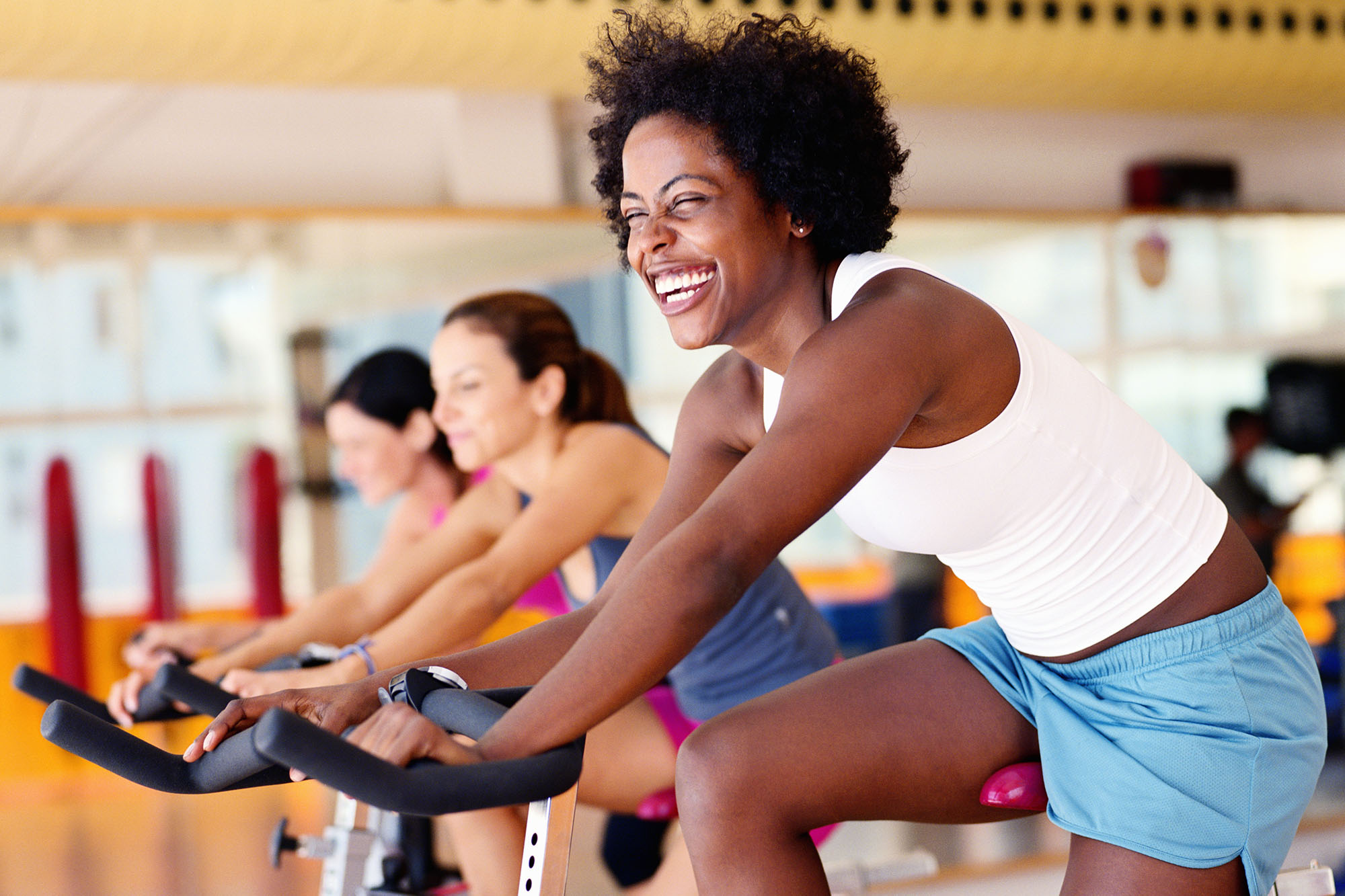Women sitting on exercising bikes in gym, side view