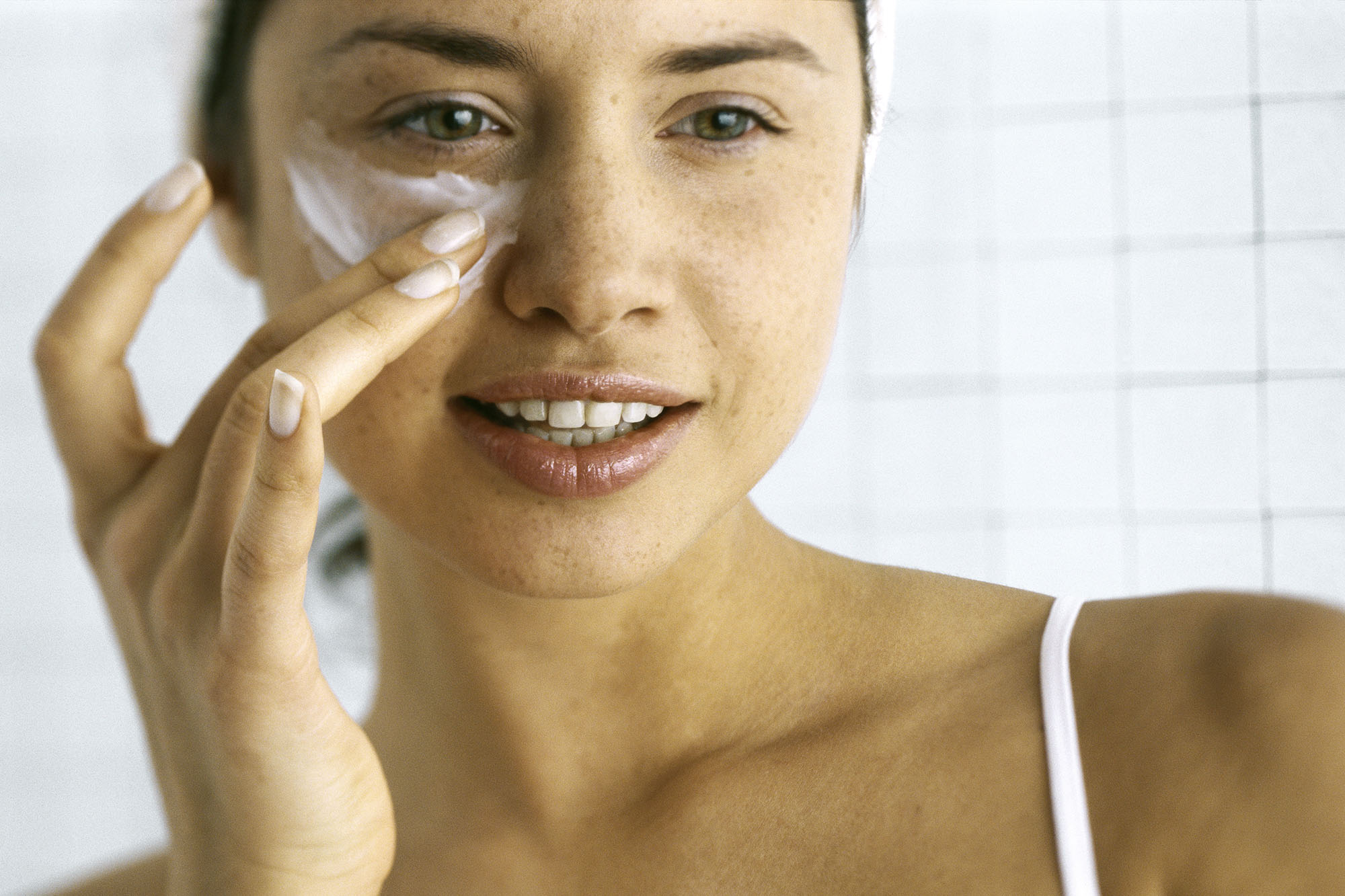Woman applying moisturizer beneath eye
