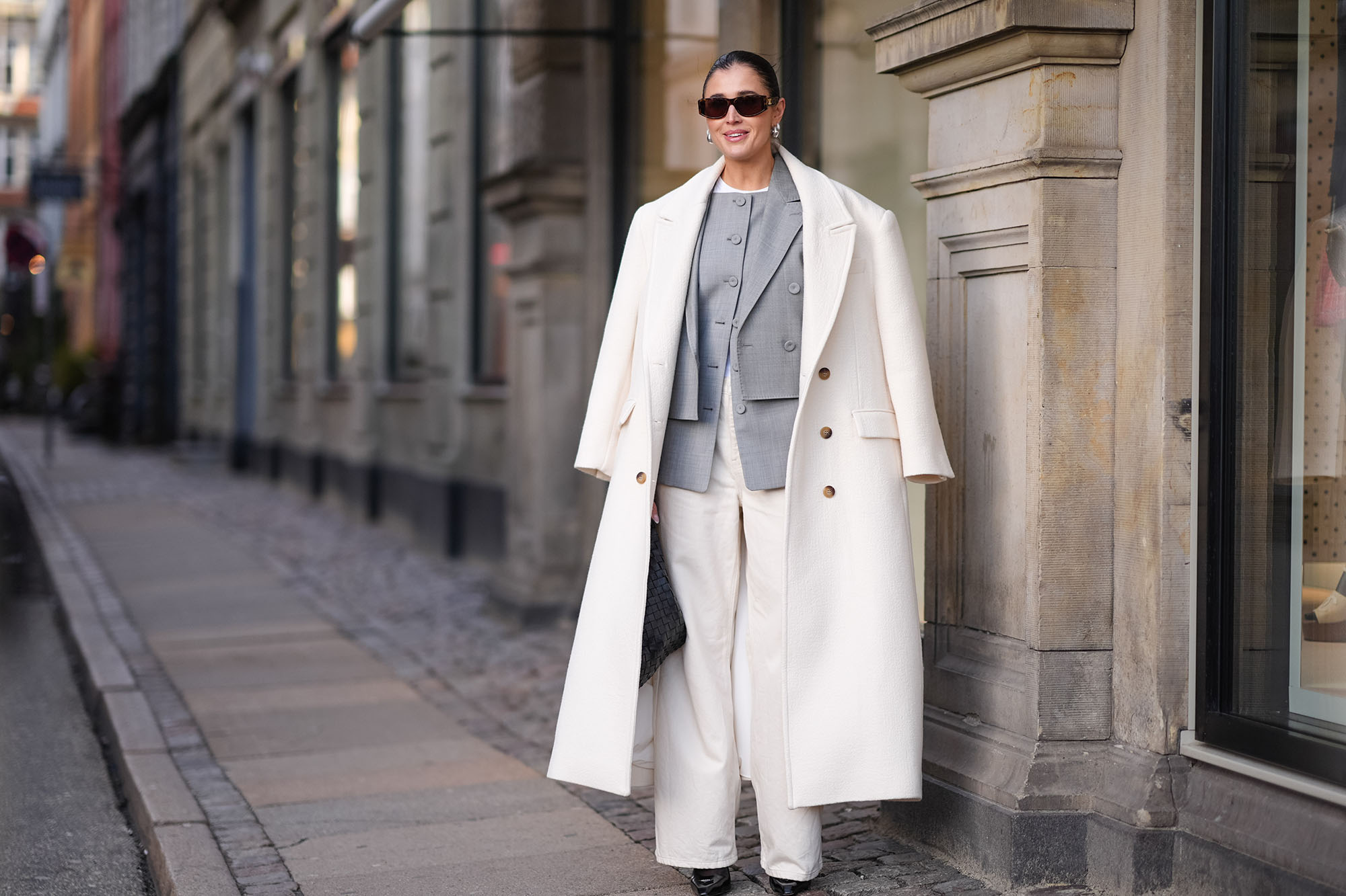 Inspiration shot: Darja Barannik wears sunglasses, golden earrings, a white oversized long coat, a gray oversized blazer jacket , white flared suit pants , pointed shoes, a black woven leather Bottega Veneta bag, outside Mark Kenly Domino Tan, during the Copenhagen Fashion Week AW24 on February 01, 2024 in Copenhagen, Denmark. (Photo by Edward Berthelot/Getty Images)