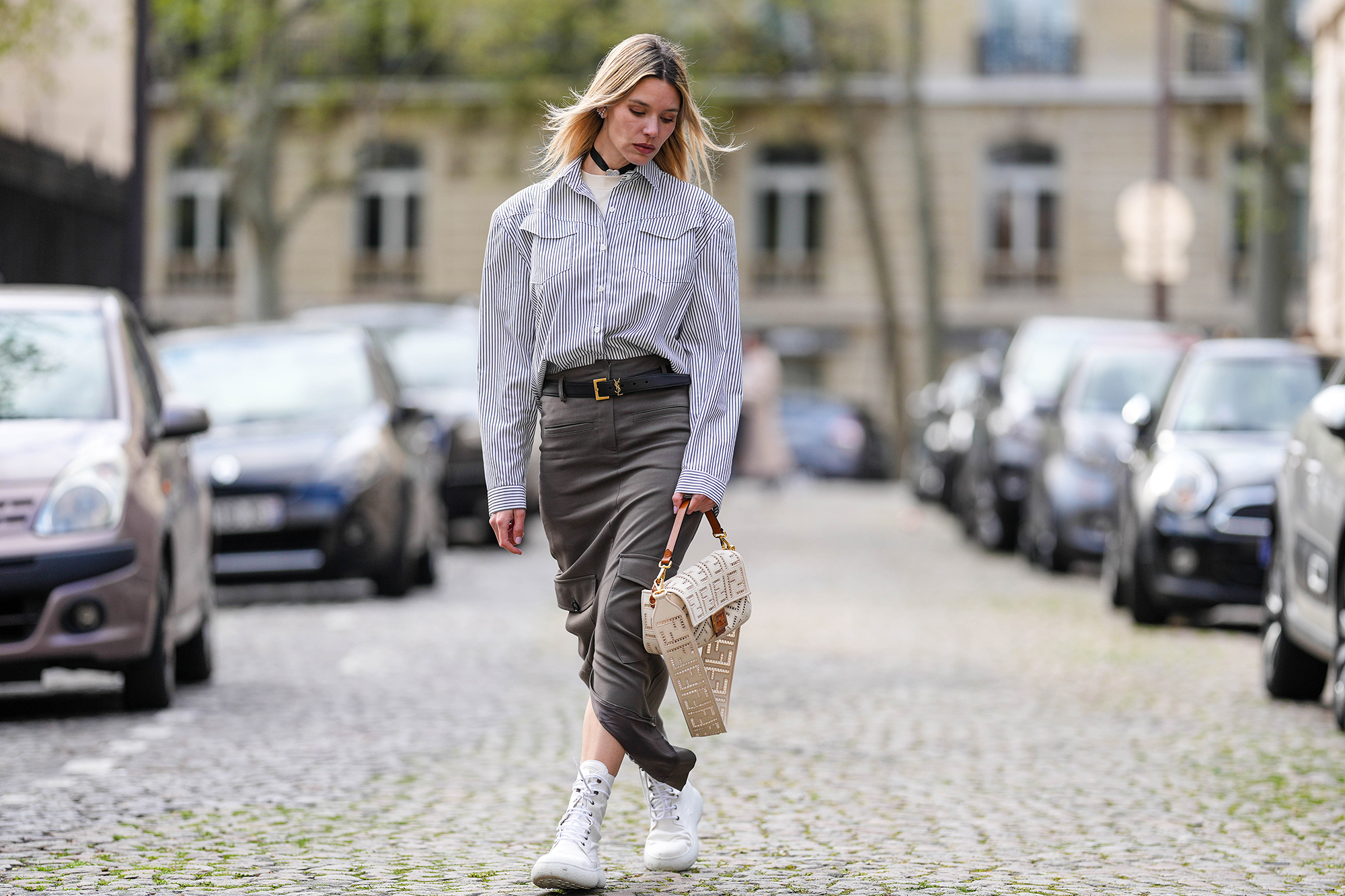 PARIS, FRANCE - APRIL 15: Natalia Verza wears diamonds earrings, a white with small black striped print pattern shirt, a white latte matte leather with cut-out FF monogram pattern crossbody bag from Fendi, a black shiny leather small belt, a dark gray long slit / split skirt, white platform soles ankle boots , during a street style fashion photo session, on April 15, 2023 in Paris, France. (Photo by Edward Berthelot/Getty Images)