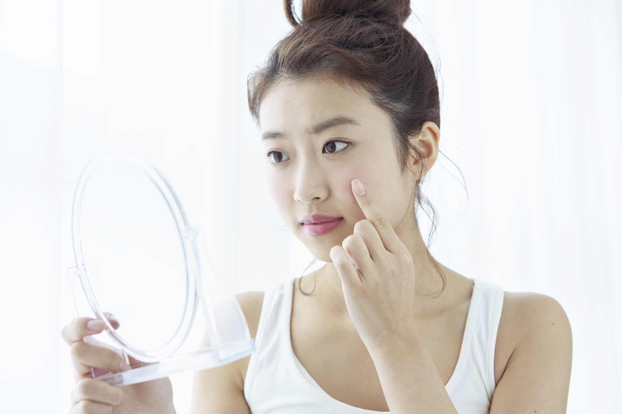 Young woman looking at her cheek in hand mirror