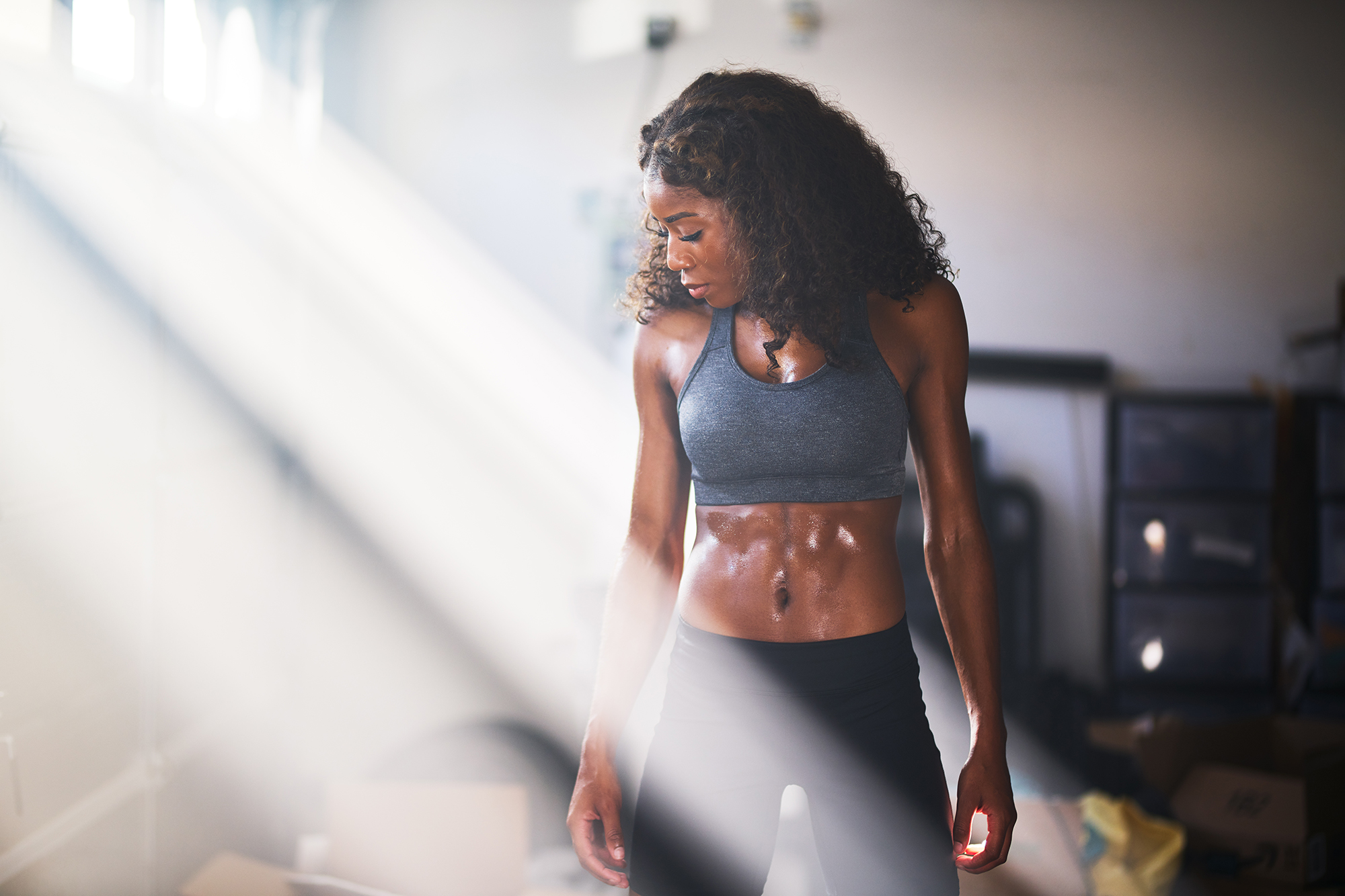 Muscular woman sweating from work out in home gym with light rays