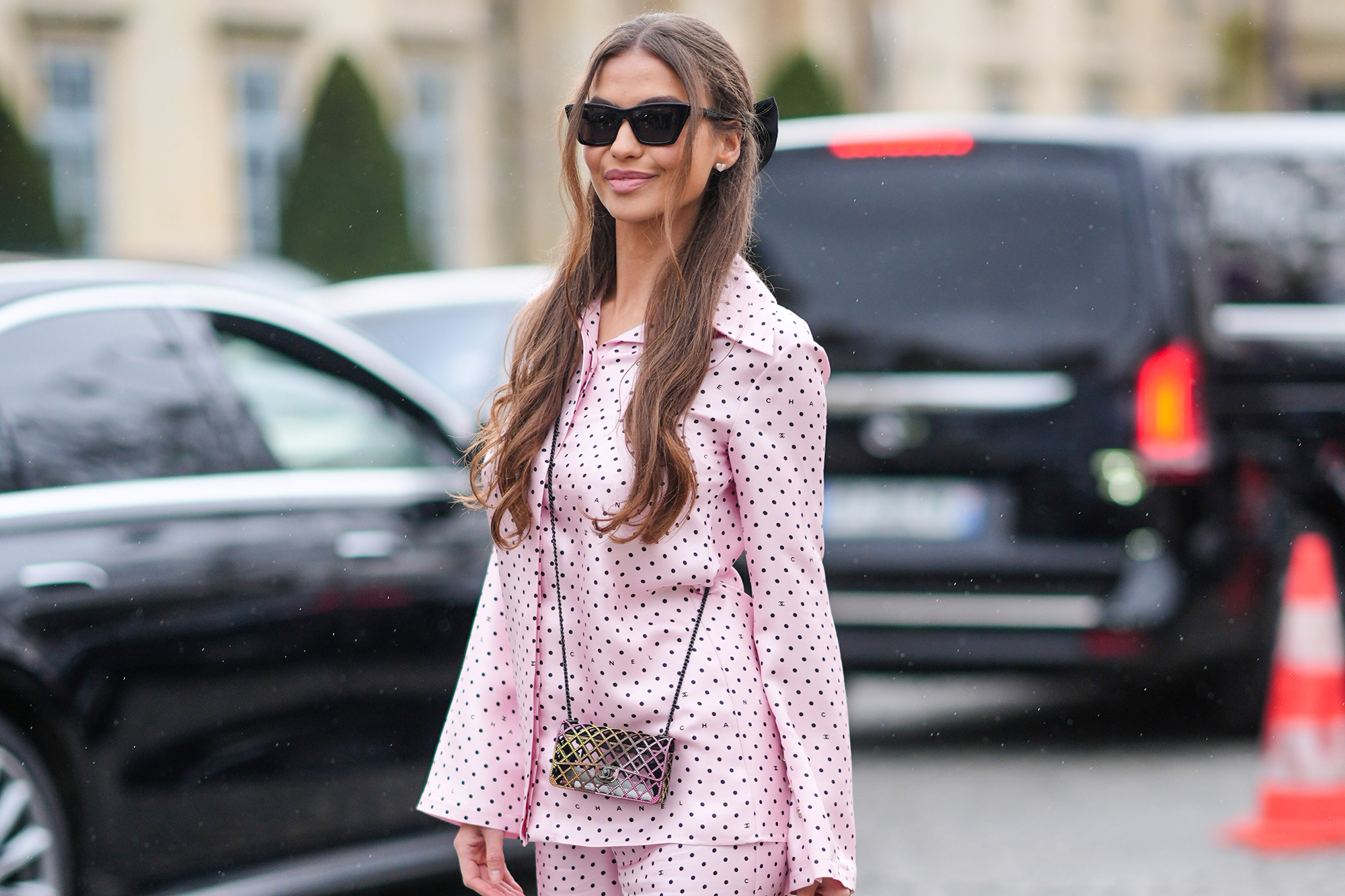 A guest wears sunglasses, a pink Chanel pajama with flared pants and printed polka dots, a Chanel bag, platform shoes, outside Chanel, during the Womenswear Fall/Winter 2024/2025 as part of Paris Fashion Week on March 05, 2024 in Paris, France.