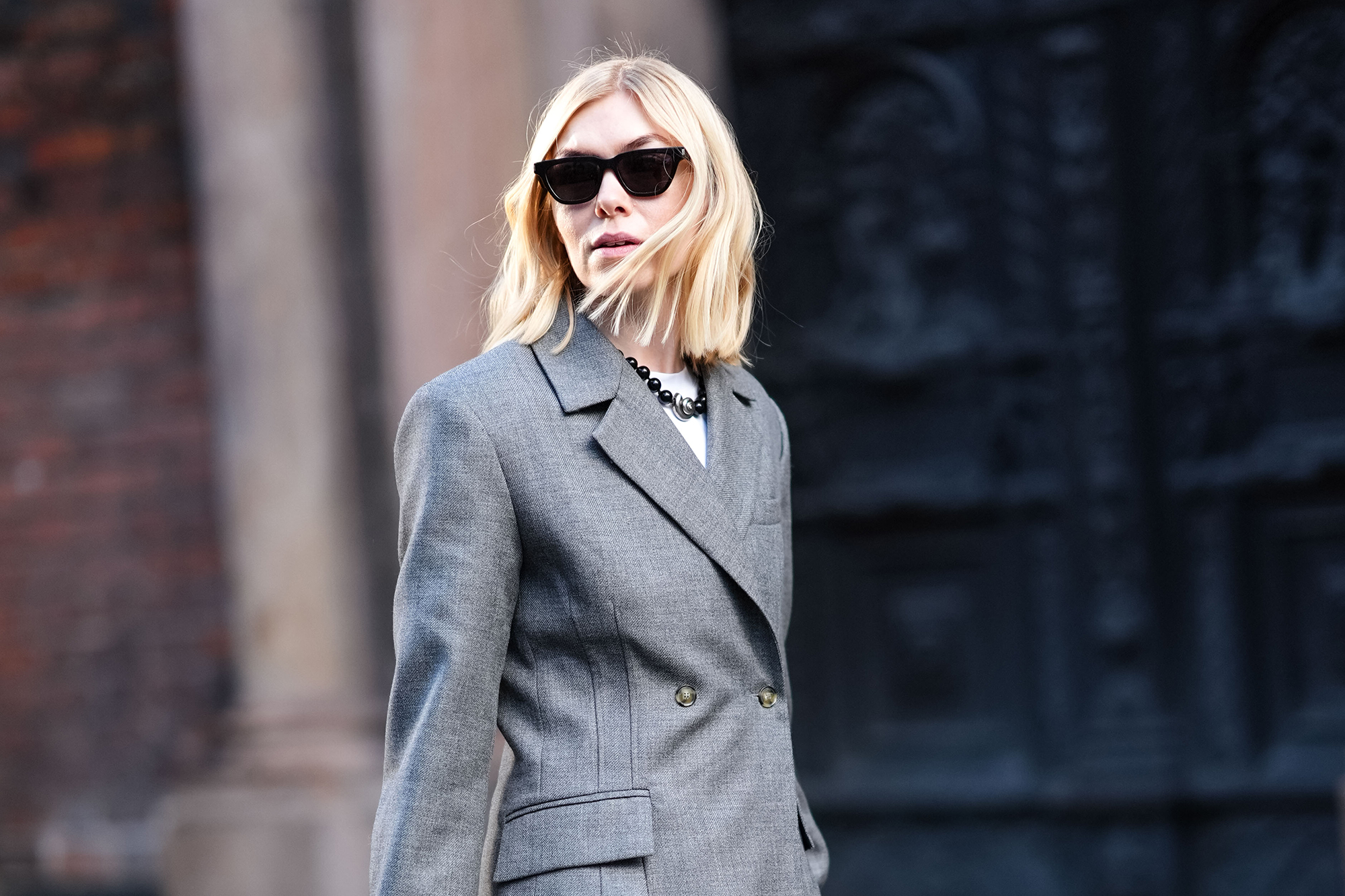 A guest wears sunglasses, a gray oversized blazer jacket , suit flared pants , shiny sequined shoes, a black woven leather Bottega Veneta bag, outside Herskind, during the Copenhagen Fashion Week FW24 on January 31, 2024 in Copenhagen, Denmark.