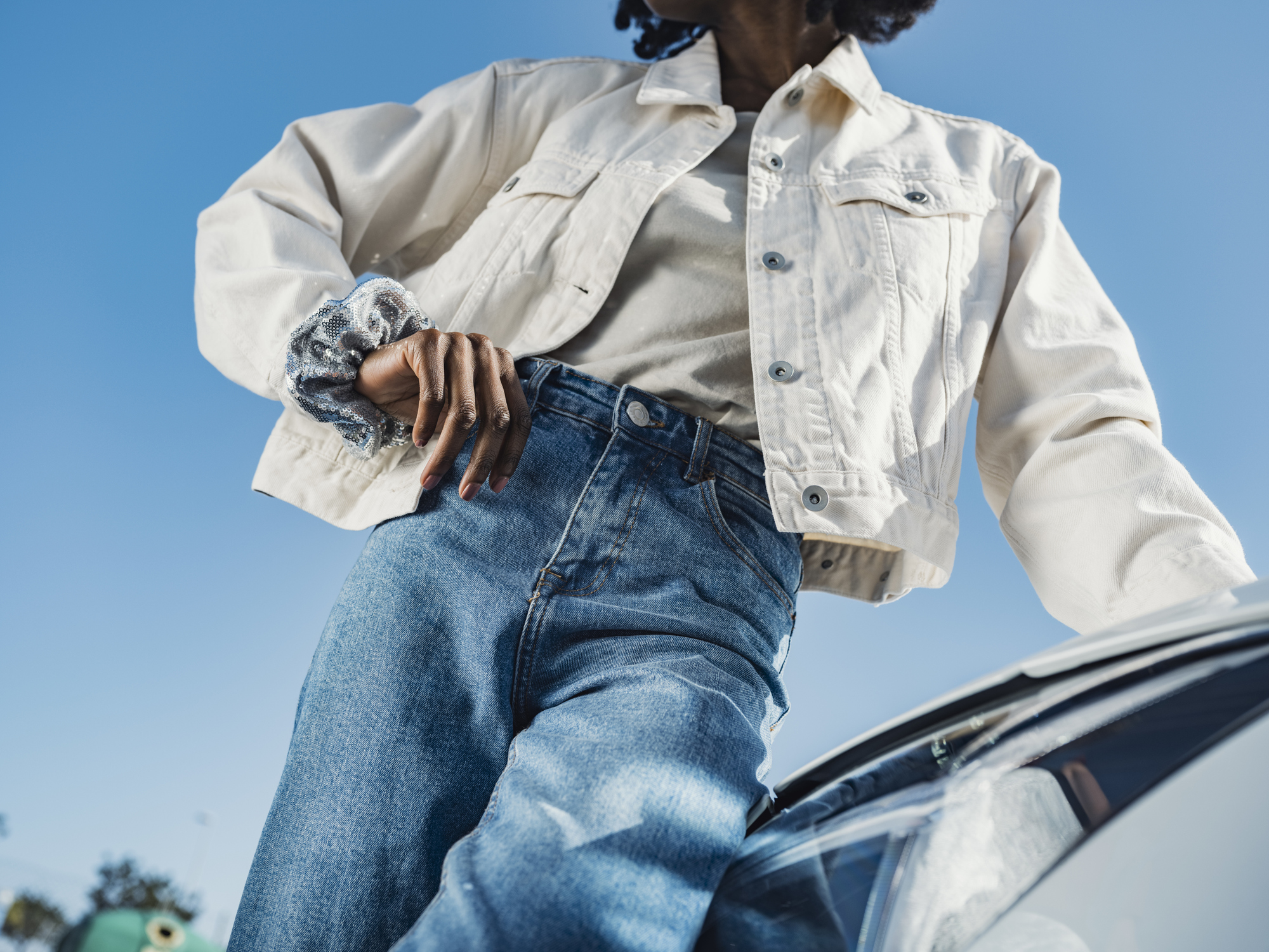 Young woman leaning on car headlight in front of sky