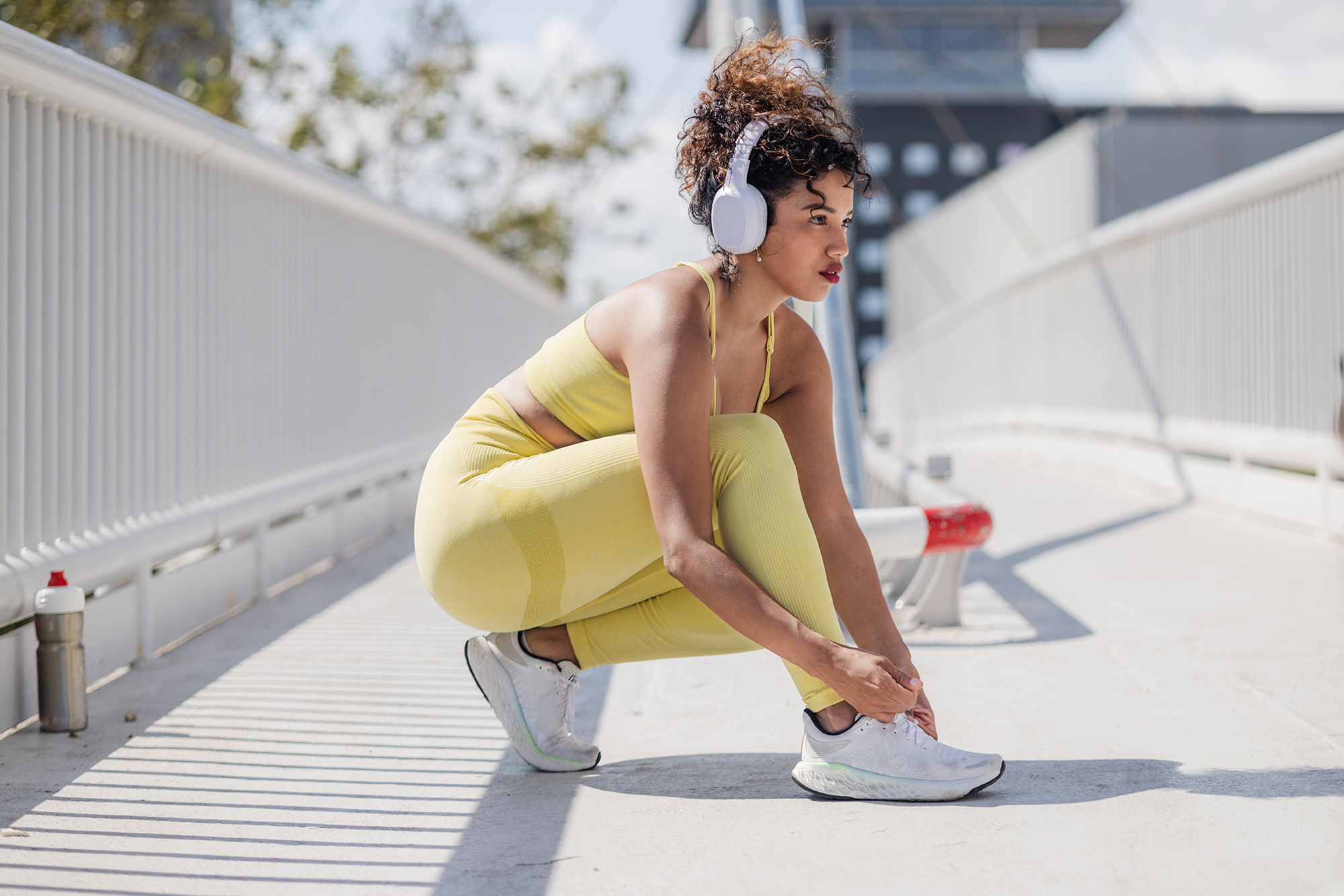 A young woman with wireless headphones tying shoelaces on her trainers before running