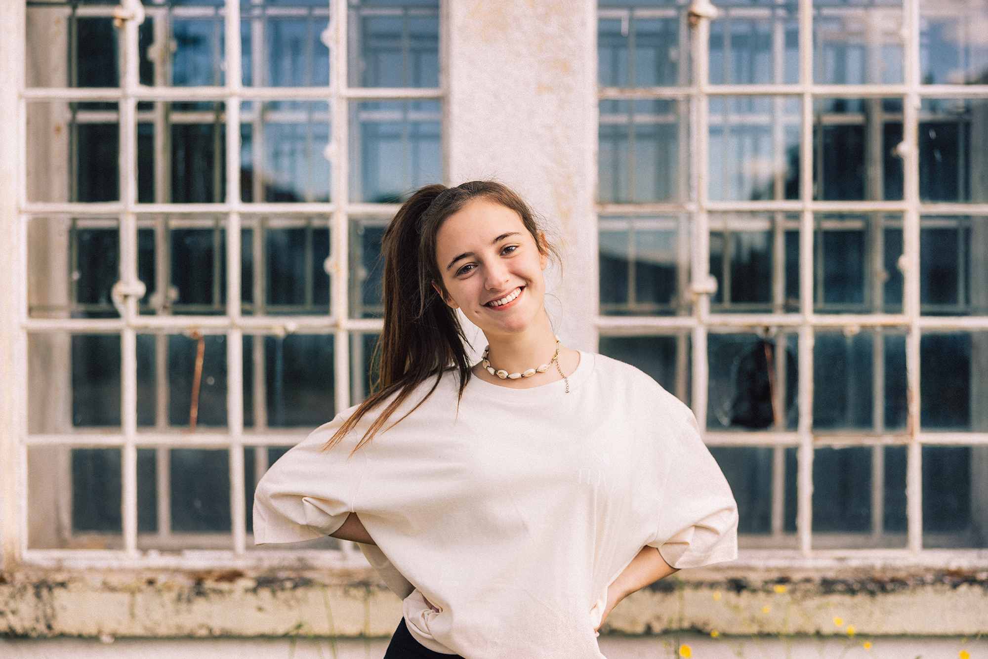 Young fashionable woman with ponytail wearing property released handmade craft designer T-Shirt Standing looking towards the Camera. Majestic industrial Window in the background. Millennial Generation Girl Young Fashion Design Portrait.