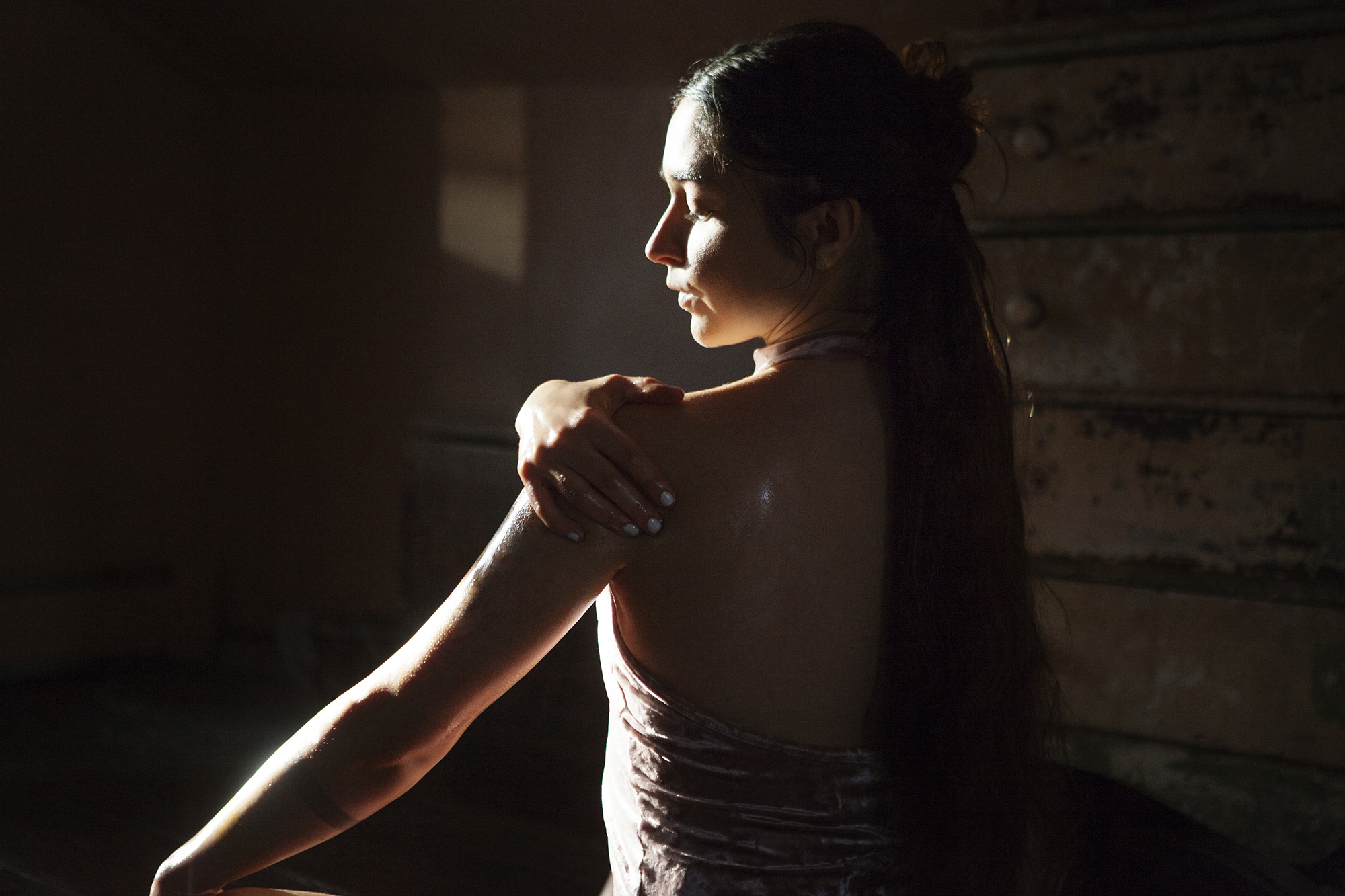 Rear view of woman applying oil to body in dark room at home