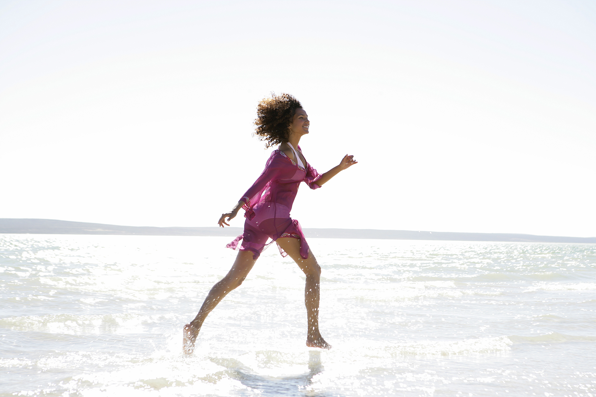 Woman in bikini and cover-up running in ocean