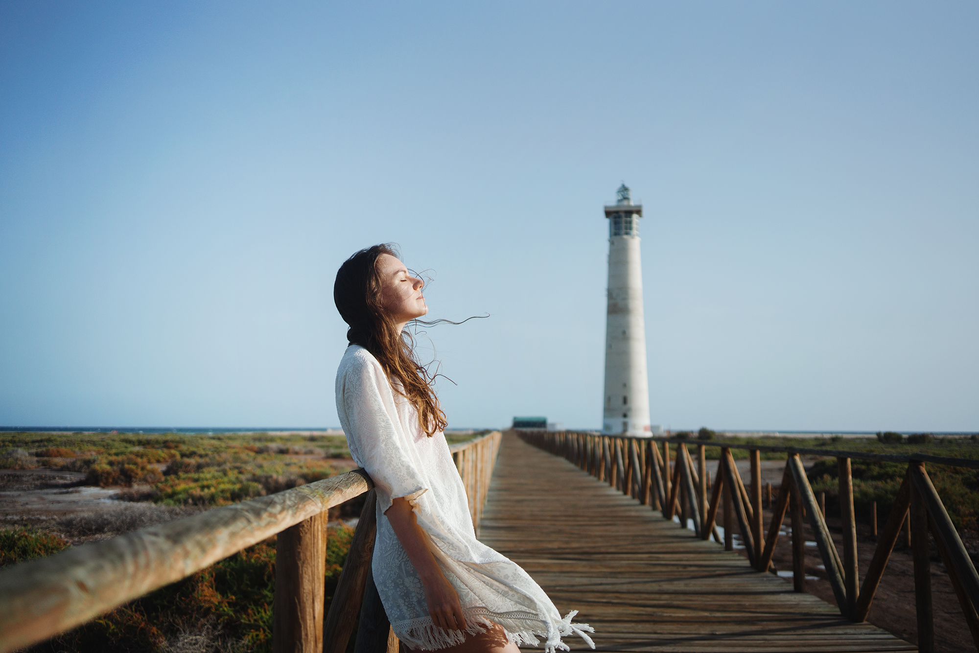 Young contemplating nature at the beach with a lighthouse in the background - hope concept