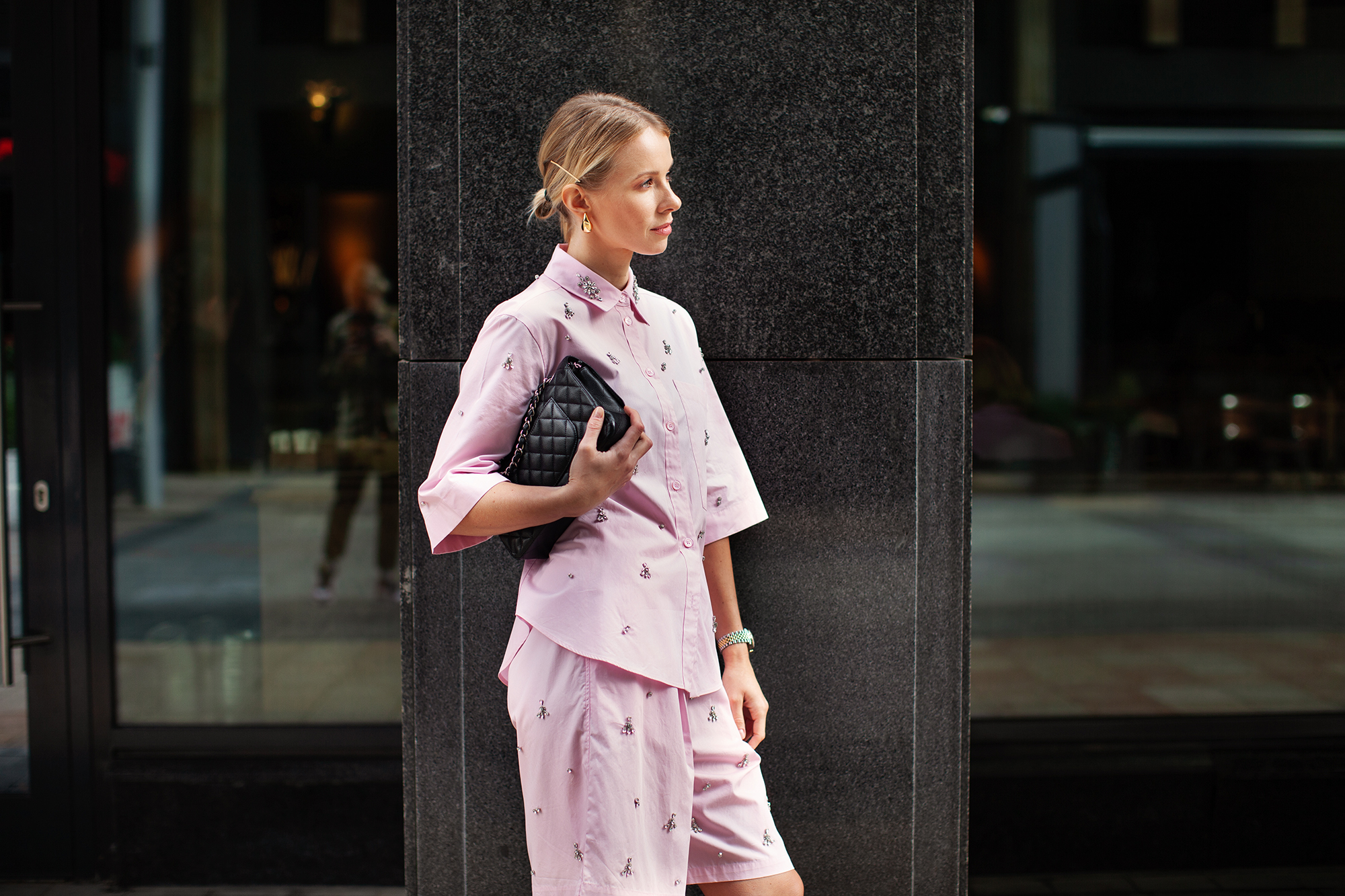 Stylish fashion woman wearing pink suit, shirt and shorts, standing confidently against a city backdrop. Urban street style allure.
