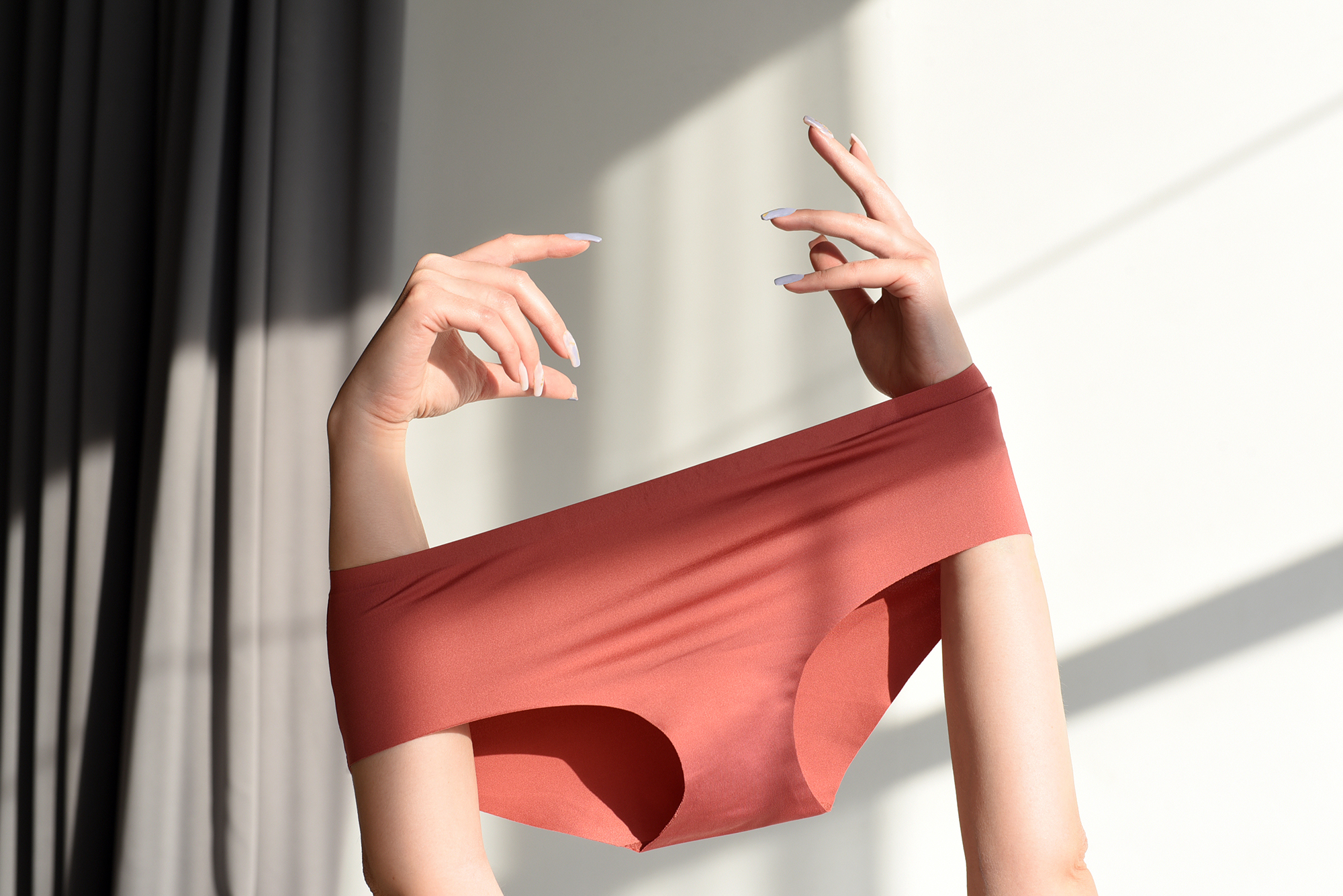 Seamless female panties in the hands of the girl. White background with sun shadow.