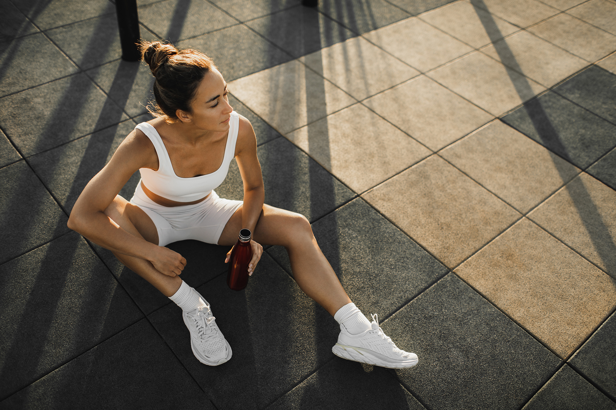 Sportive woman with slim tanned body relaxing after fitness training on outdoors sports ground. Taking a break to drink cold water and refresh. Sports hobby, healthy and active lifestyle concept.