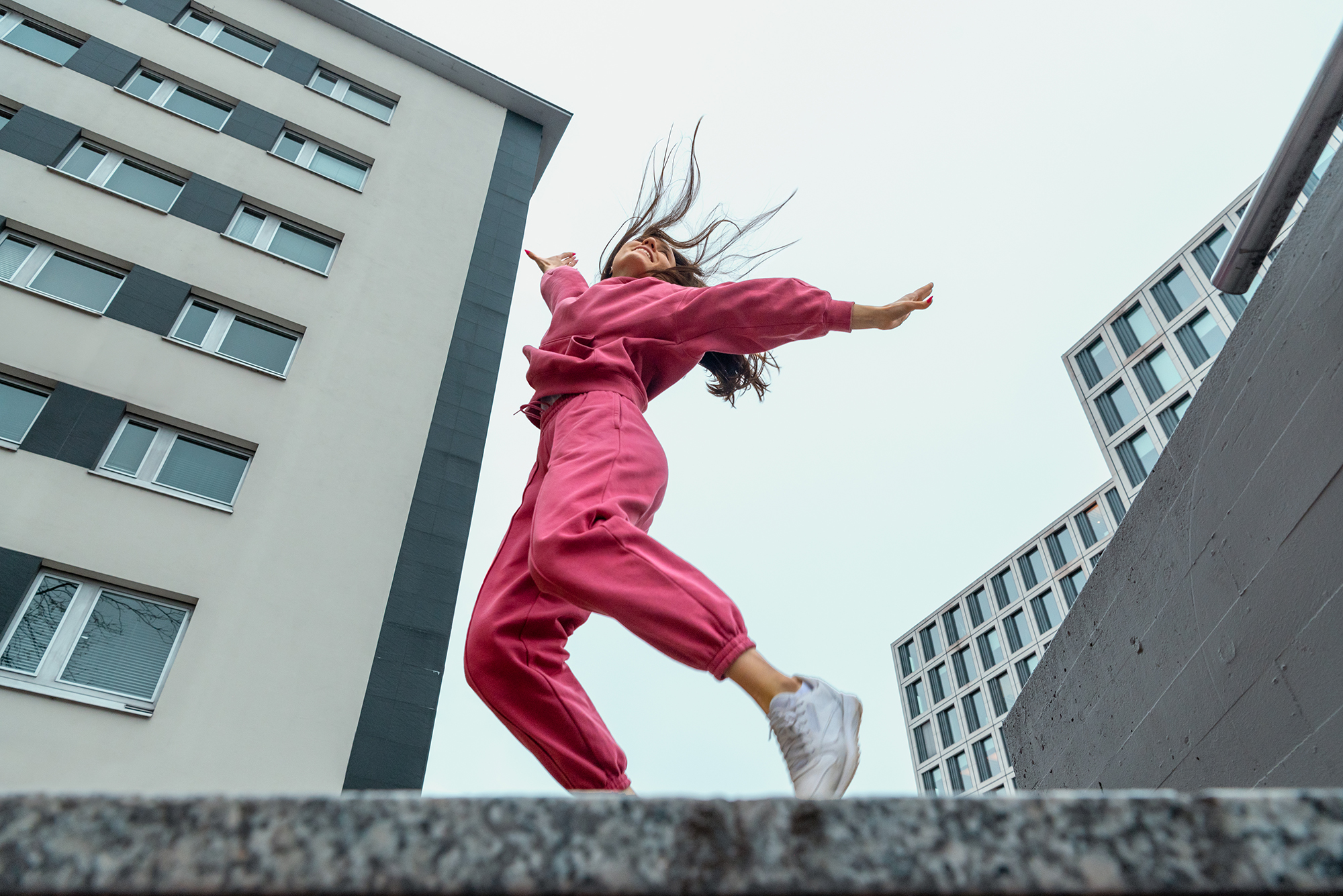 Low angle view with a happy millennial woman, dressed in a pink sport outfit smiling and raising the arms.