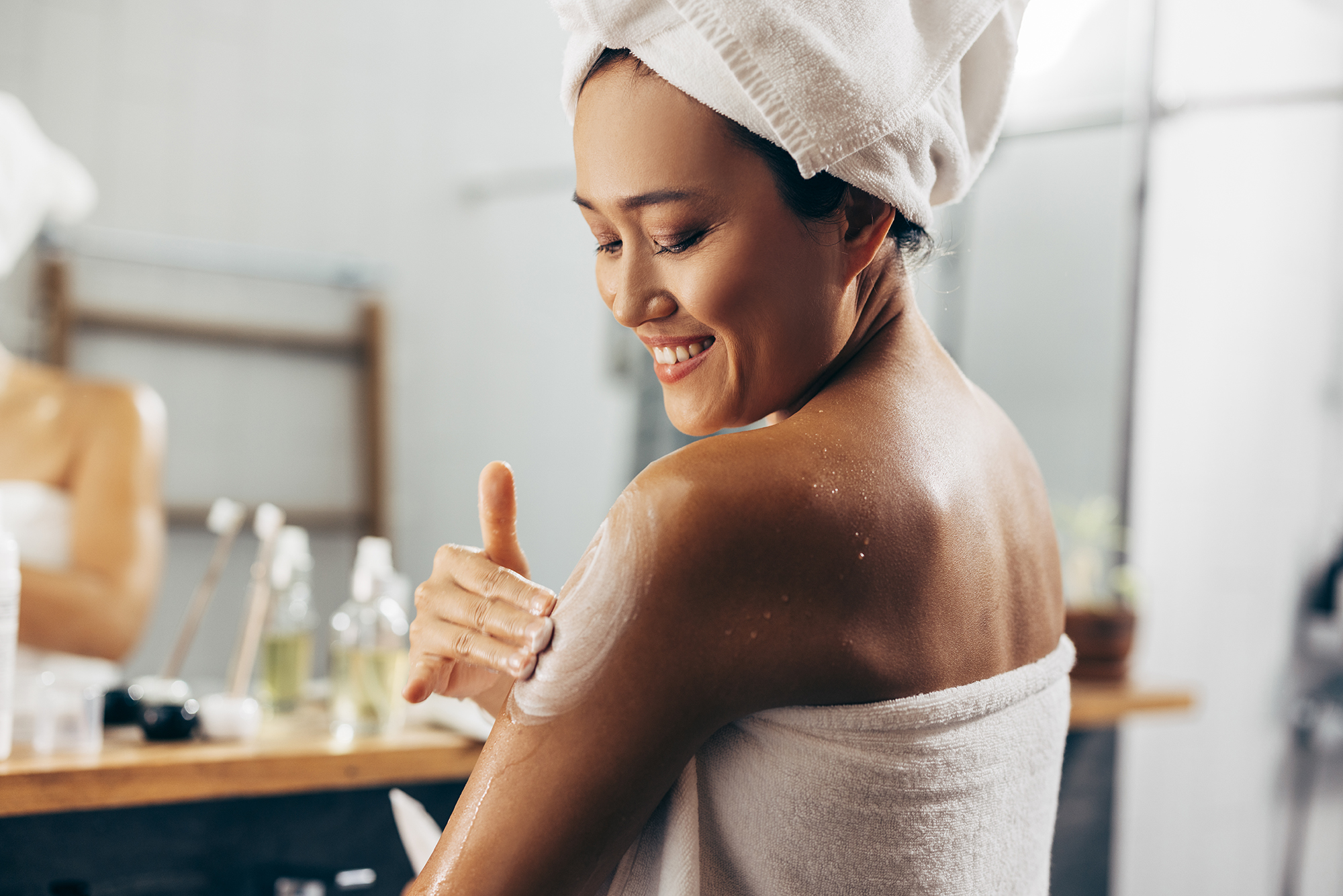 Young woman following her skin care routine, she is applying the cream after a shower.