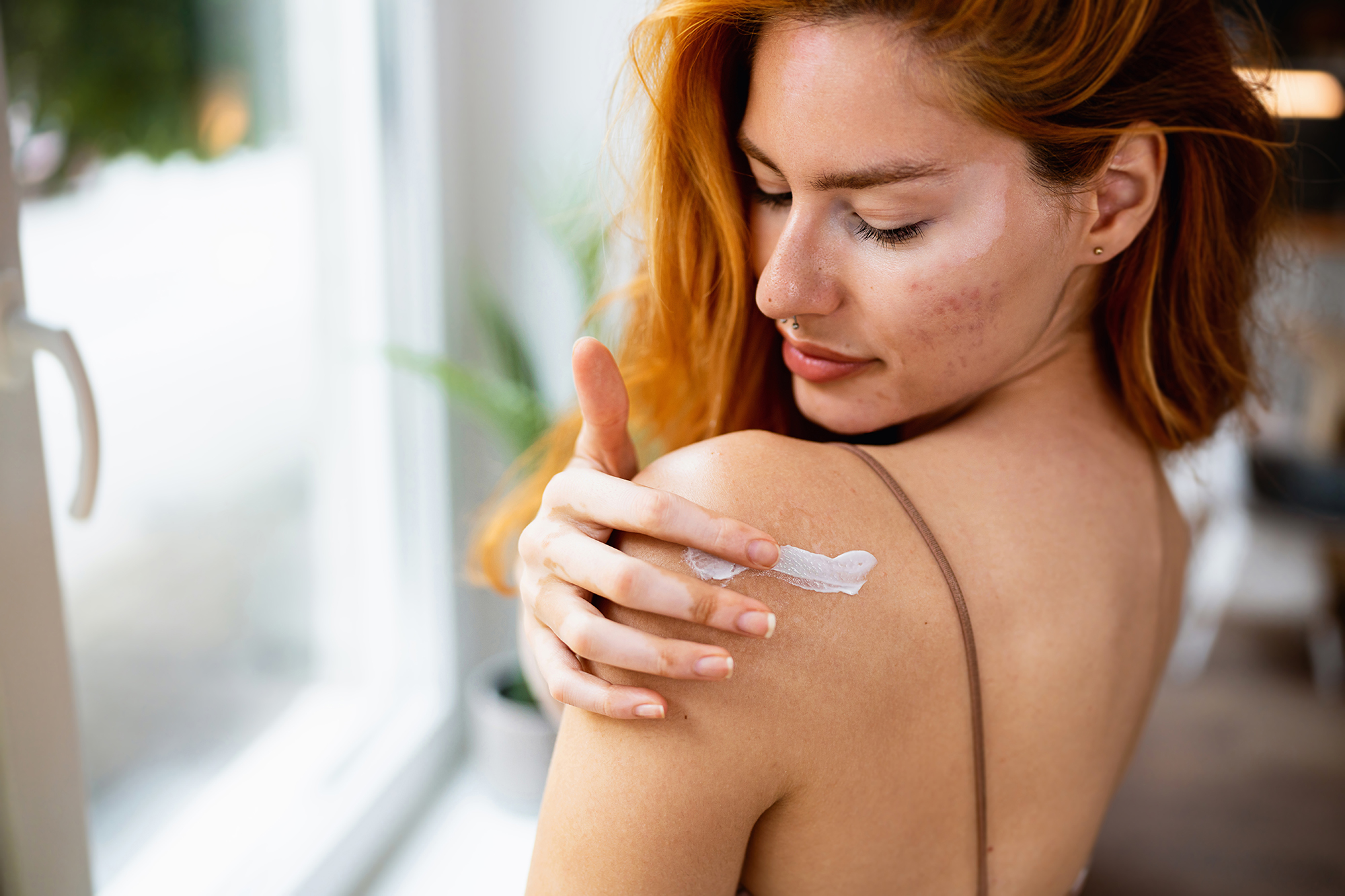 Young redhead woman applying body cream on shoulder