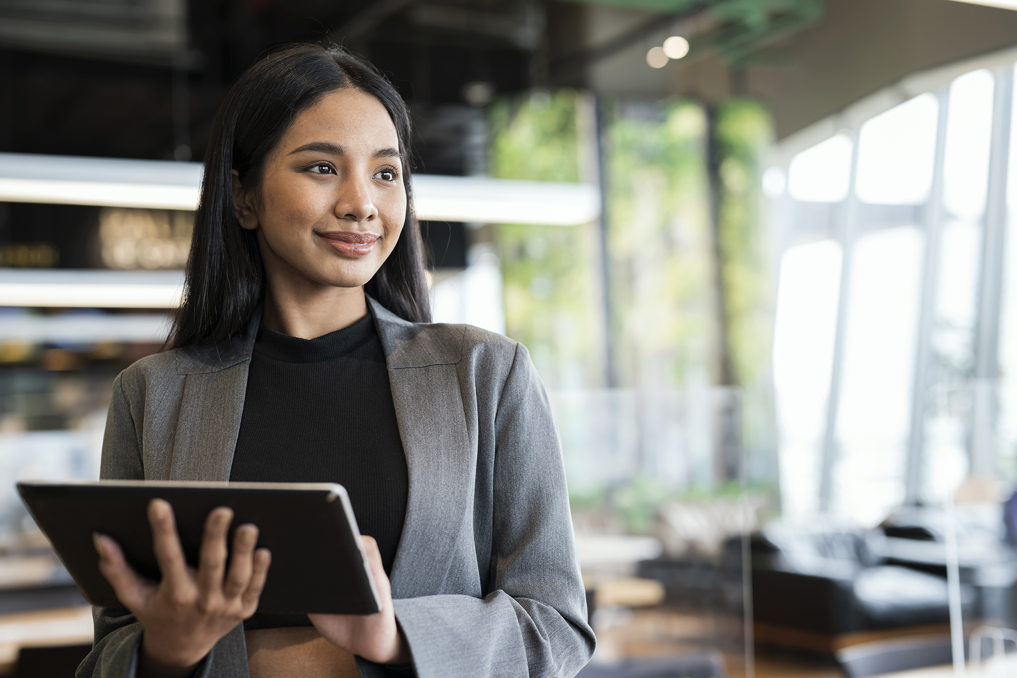 Businesswomen using a tablet while standing and looking away in a financial business office.