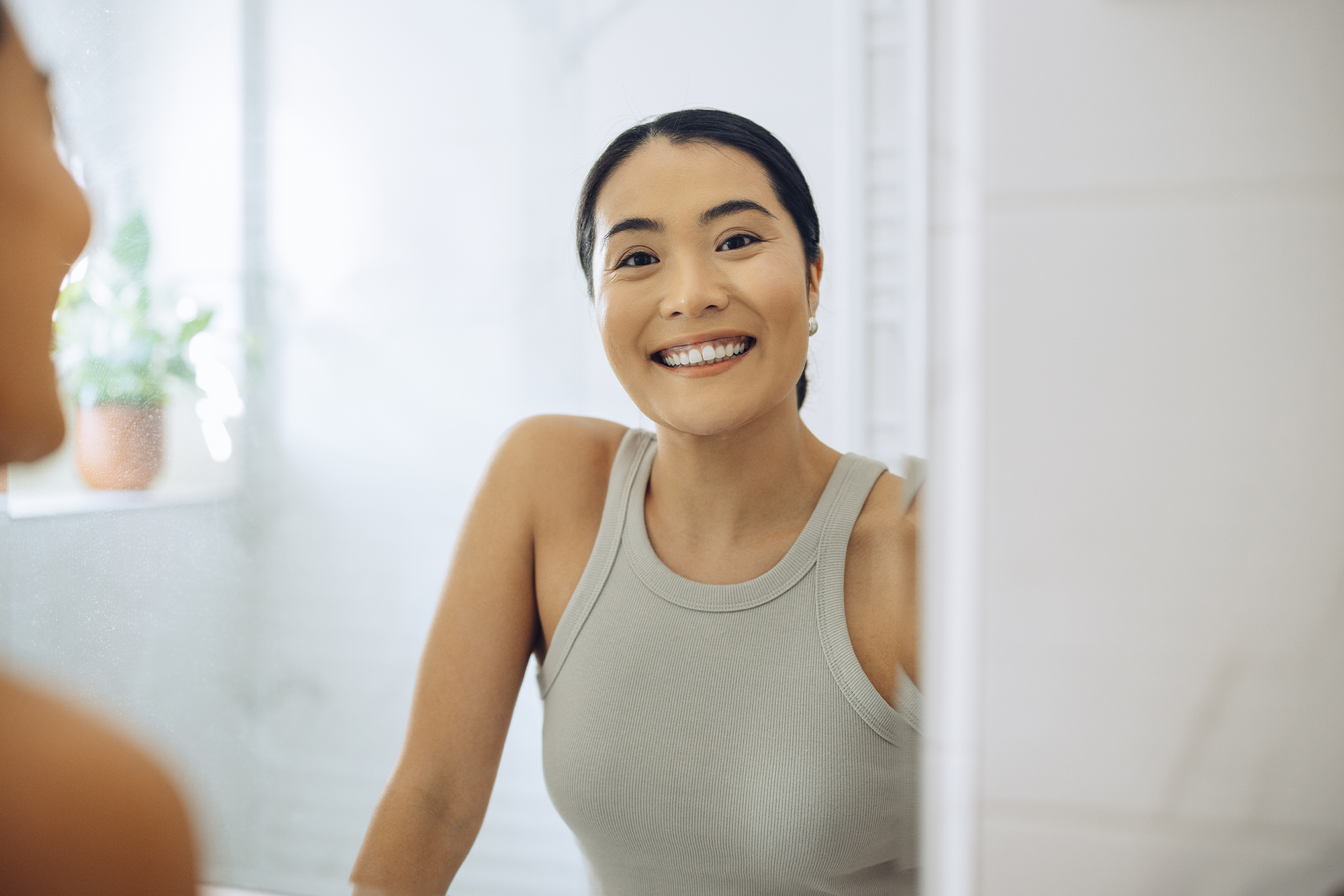 Cheerful Woman standing at her sink in the bathroom, looking at herself in the mirror.