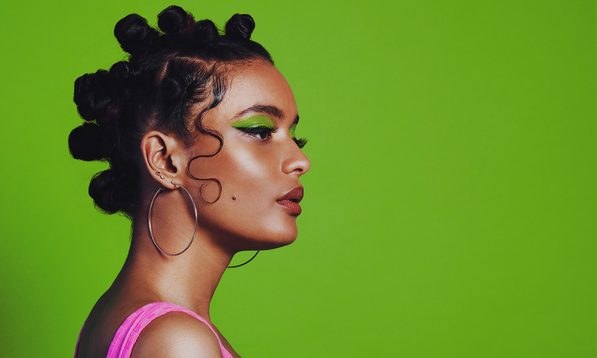 Shot of a woman posing against a green background with her bantu knots