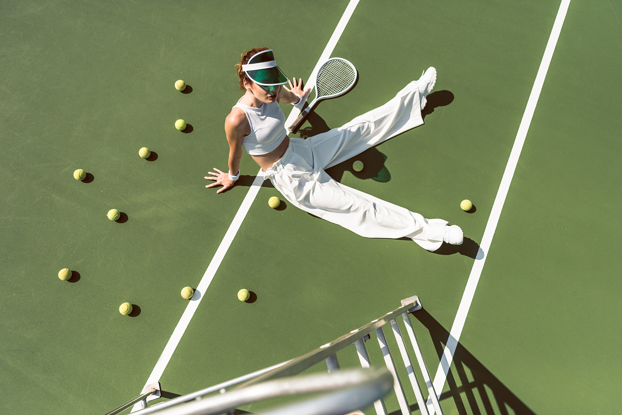 high angle view of beautiful woman in stylish white clothing sitting on tennis court with balls and racket around