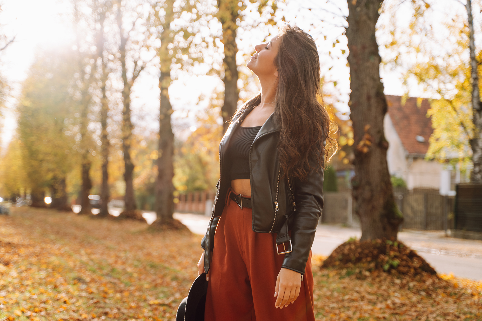 Woman standing in autumn park, breathing deeply and smiling with closed eyes