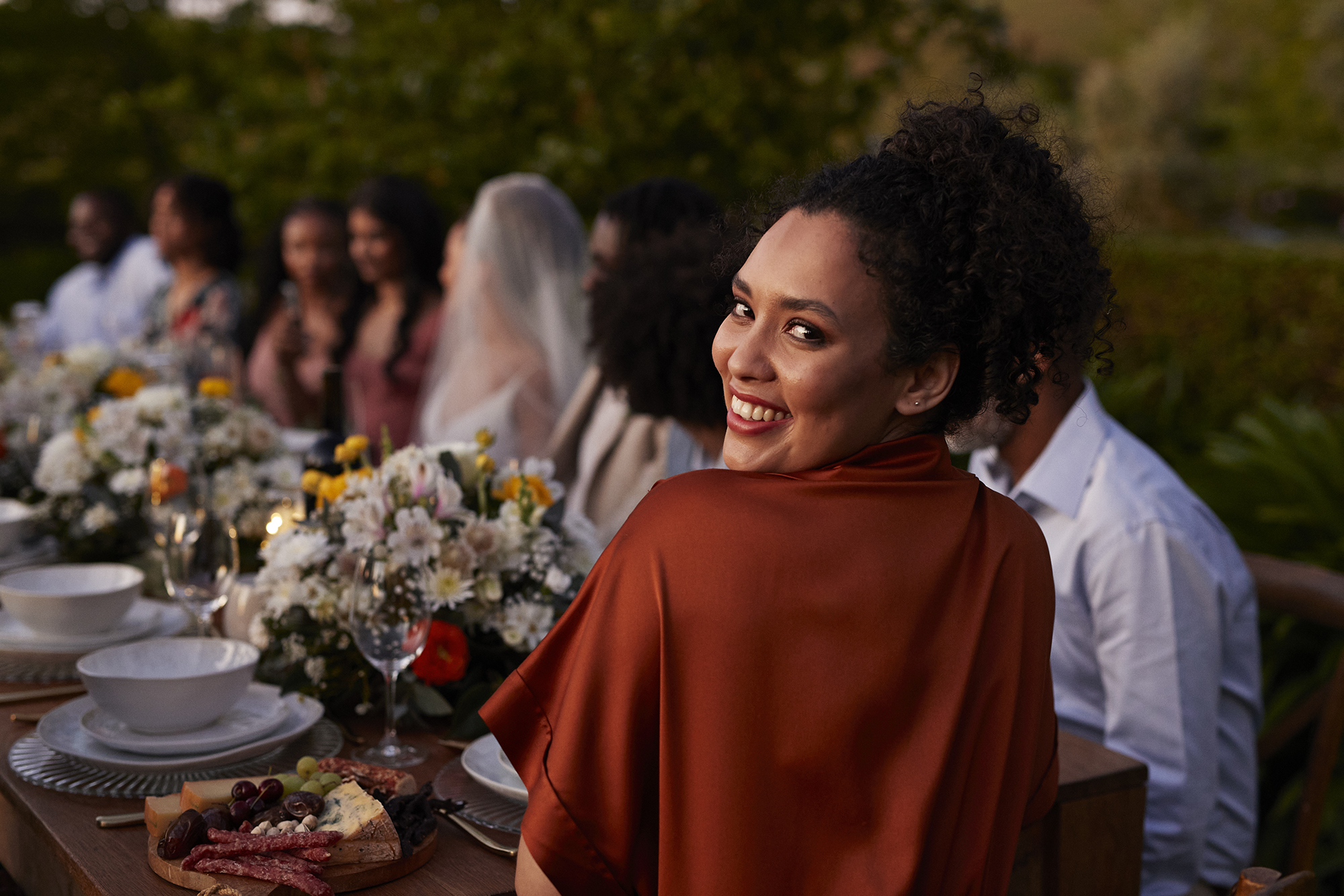 Rear view portrait of happy young woman guest looking back while sitting at dining table during wedding
