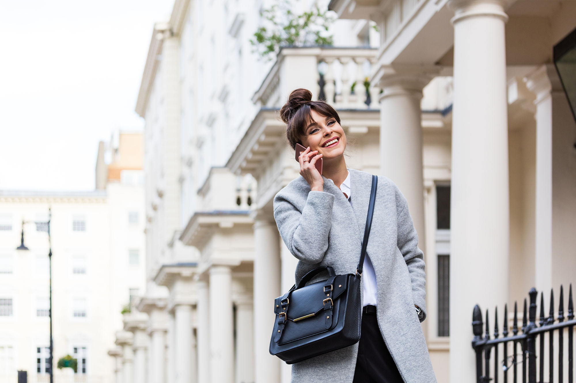 Elegant beautiful woman talking on phone in front of city houses