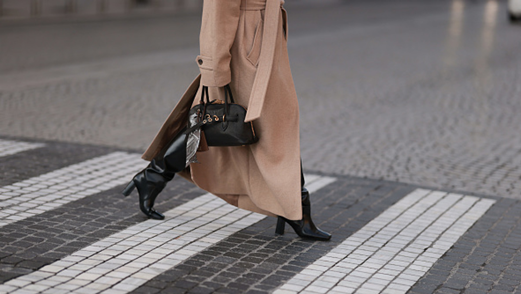 woman wearing a beige coat with boots and bag on street