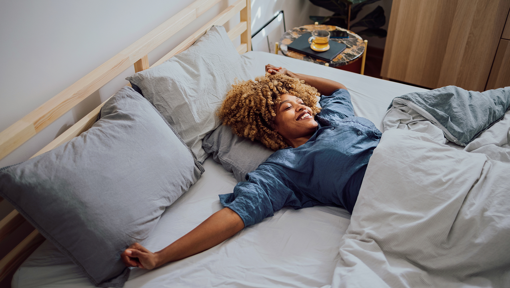 Woman is lying in her bed in the morning. She is stretching and smiling.