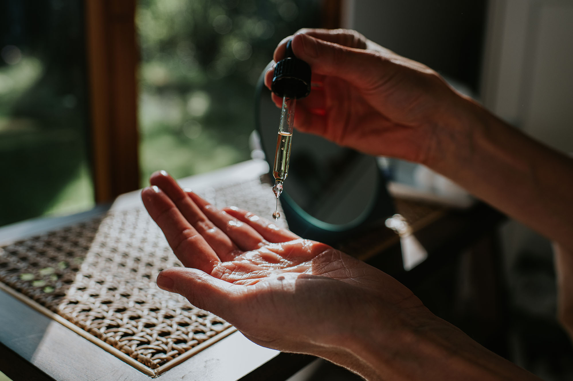 A woman in a bath robe spends some time moisturising her hands. She drops some cosmetic oil from a pipette onto the palm of her hand.