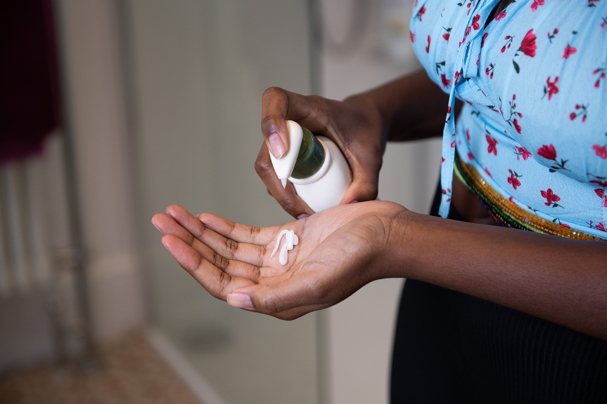 Young woman moisturising her hands and arm with cream in a domestic bathroom