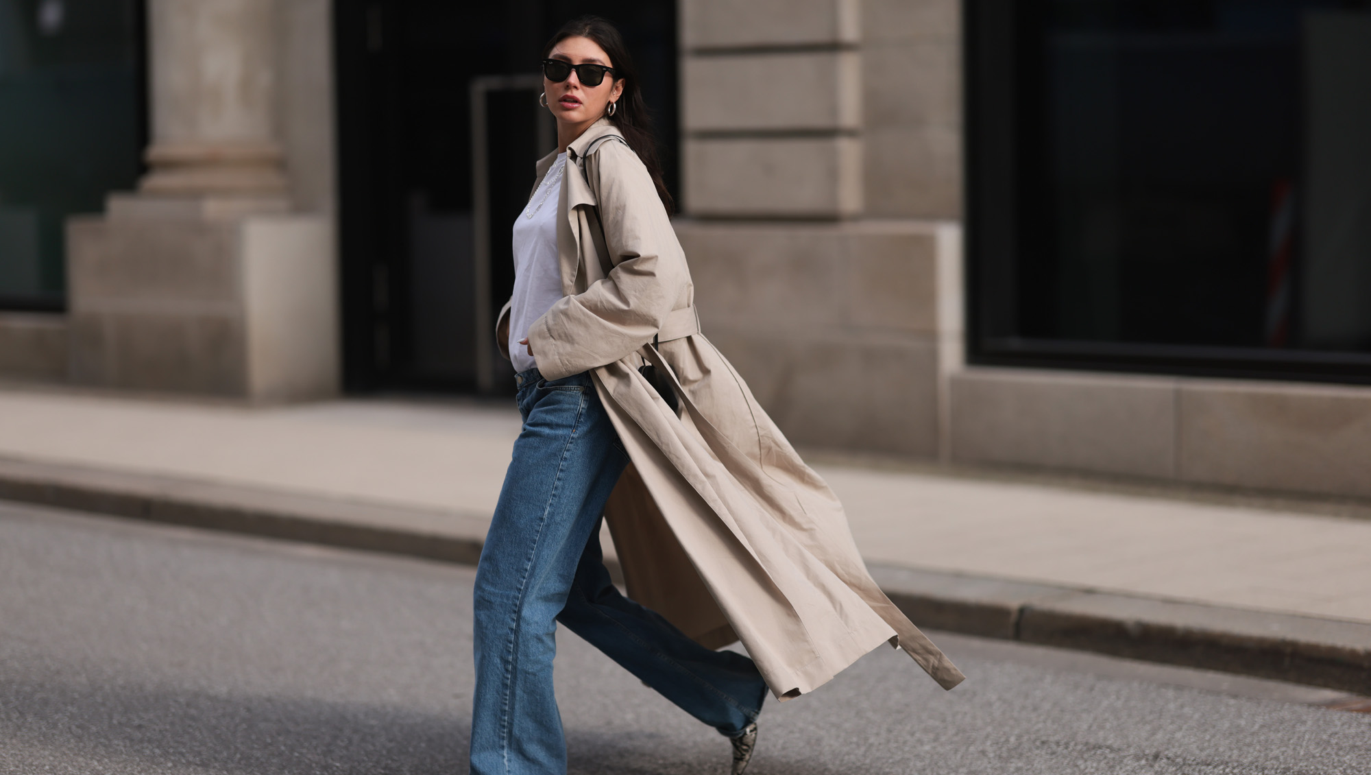Milena Karl seen wearing Ray-Ban black Wayfarer sunglasses, silver earrings, Hermès silver chain / necklace, The Row beige oversized long coat, NA-KD blue denim wide leg jeans / pants, COS white cotton basic shirt, Alaia black leather heart shaped crossbody bag and Ganni beige snake pattern leather heeled boots, on February 23, 2024 in Hamburg, Germany.