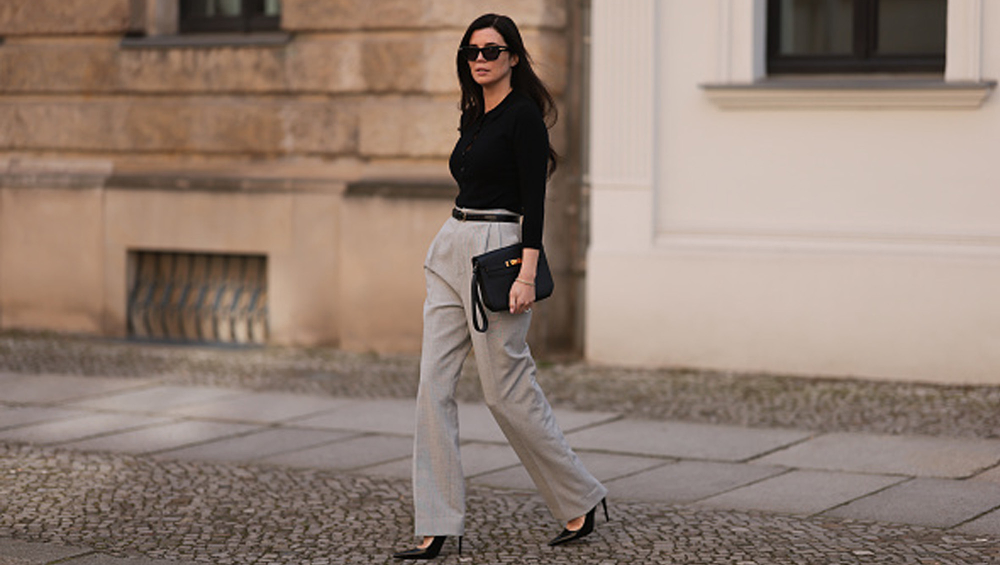 Leo Eberlin seen wearing Bottega Veneta black sunglasses, Leo Mathild jewelry / diamond bracelet and rings, Allude x Leo Mathild cashmere wool knit buttoned body, Toteme black leather belt, Velaa light grey elegant suit pants, Hermès black leather clutch bag and Saint Laurent black varnished leather heels / pumps, on February 25, 2024 in Berlin, Germany.