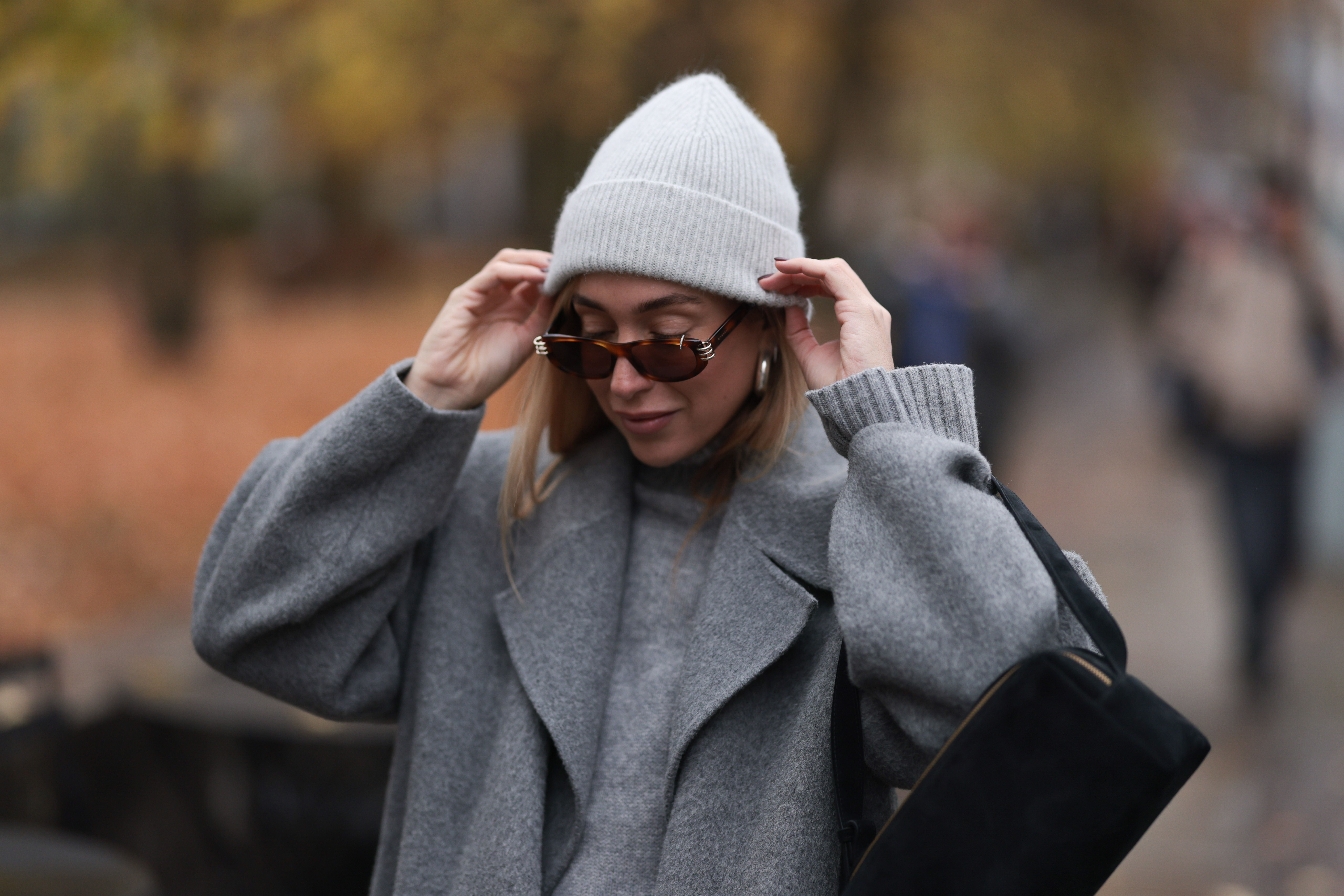 BERLIN, GERMANY - NOVEMBER 14: Sonia Lyson is seen wearing a light grey knit beanie from Le Bonnet; chunky silver hoop earrings; oval sunglasses with Havana frame and silver details from Givenchy; a calf-length grey wool coat with notch lapels from & Other Stories; a light grey knit sweater with ribbed turtleneck and cuffs from Sézane; and a rectangular black suede handbag from Elleme on November 14, 2024 in Berlin, Germany. (Photo by Jeremy Moeller/Getty Images)